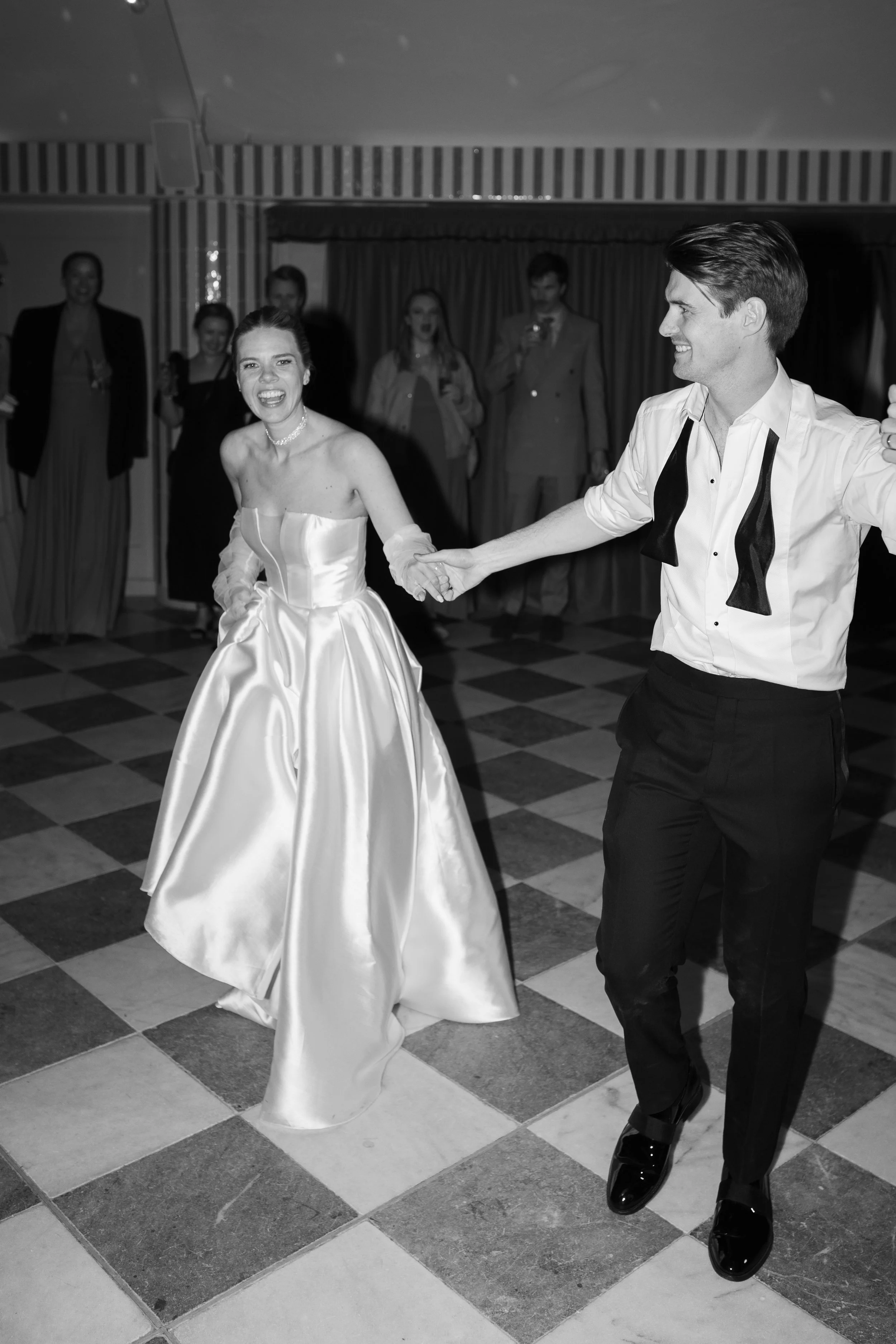 A bride and groom dancing at their wedding reception with guests in the background.