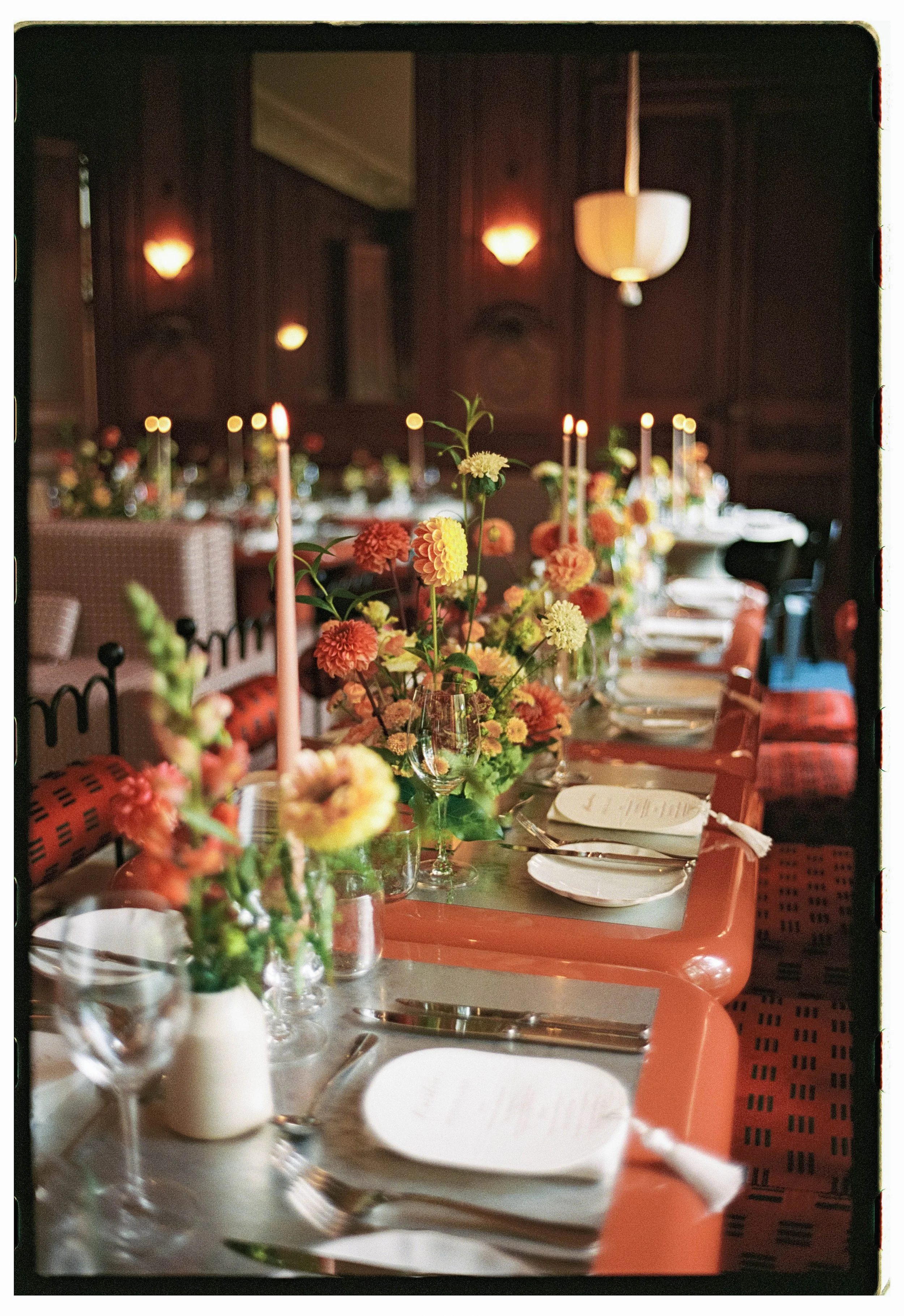 Elegant dining table set for a special occasion with floral centerpieces, candles, and place settings in a dimly lit room.