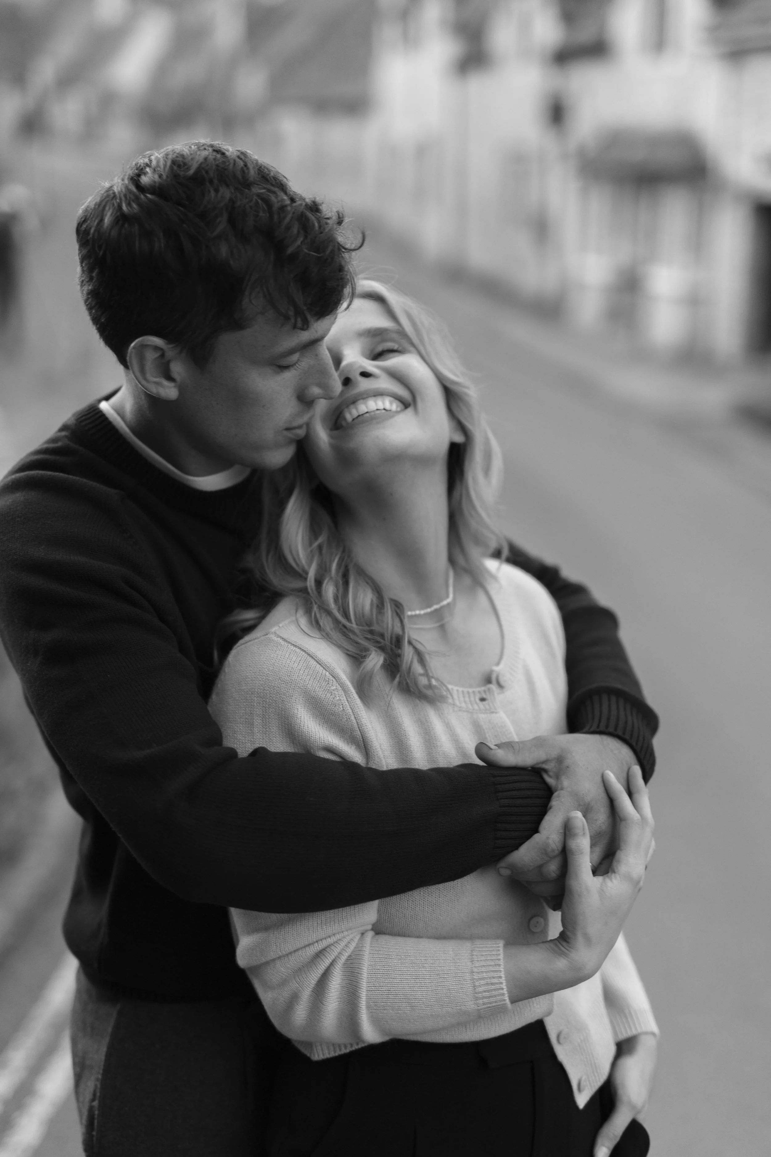 A young man hugging a smiling woman on a city street, black and white photo.