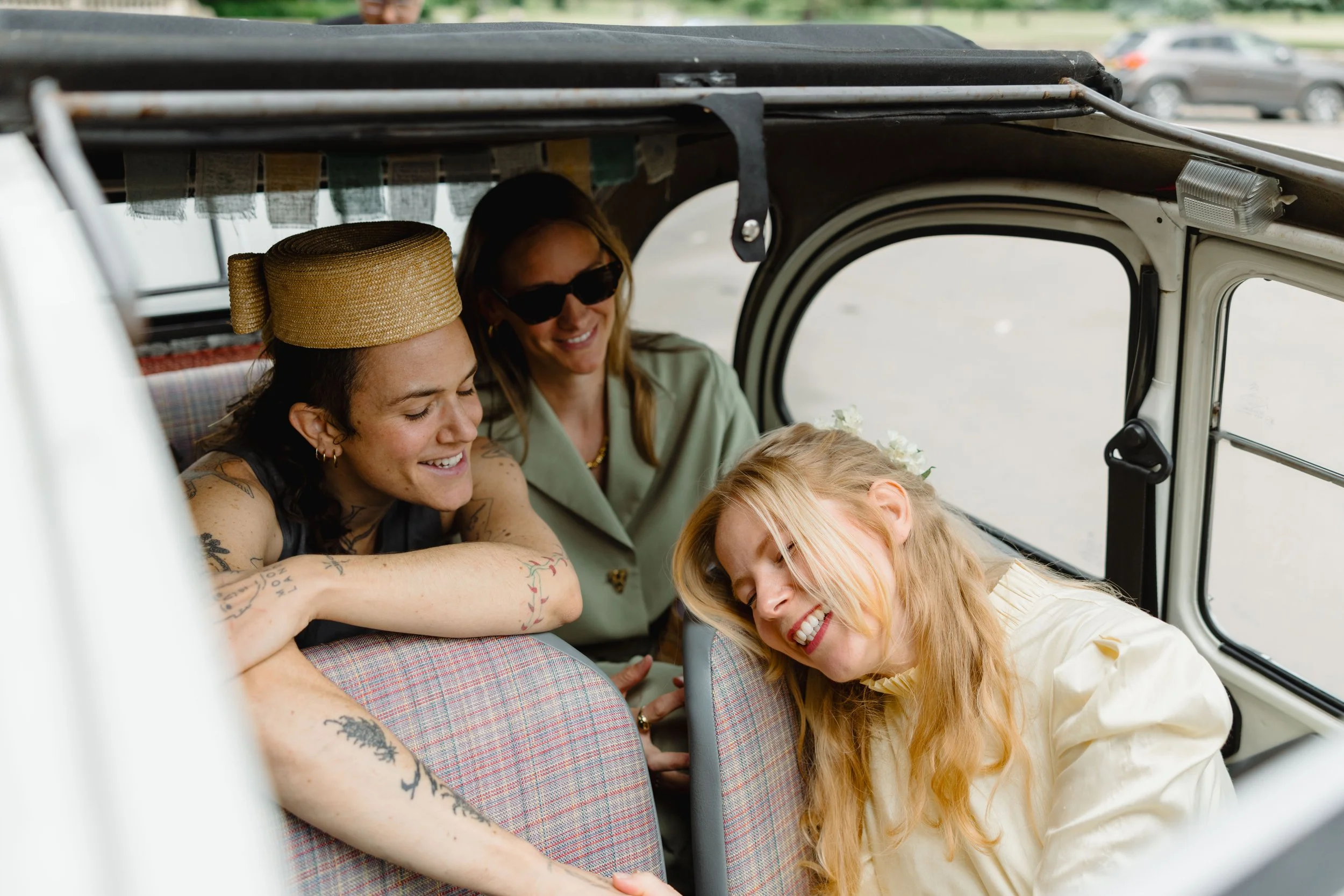 Four women sharing a joyful moment inside a vintage vehicle, with two women smiling and one leaning in with her eyes closed.