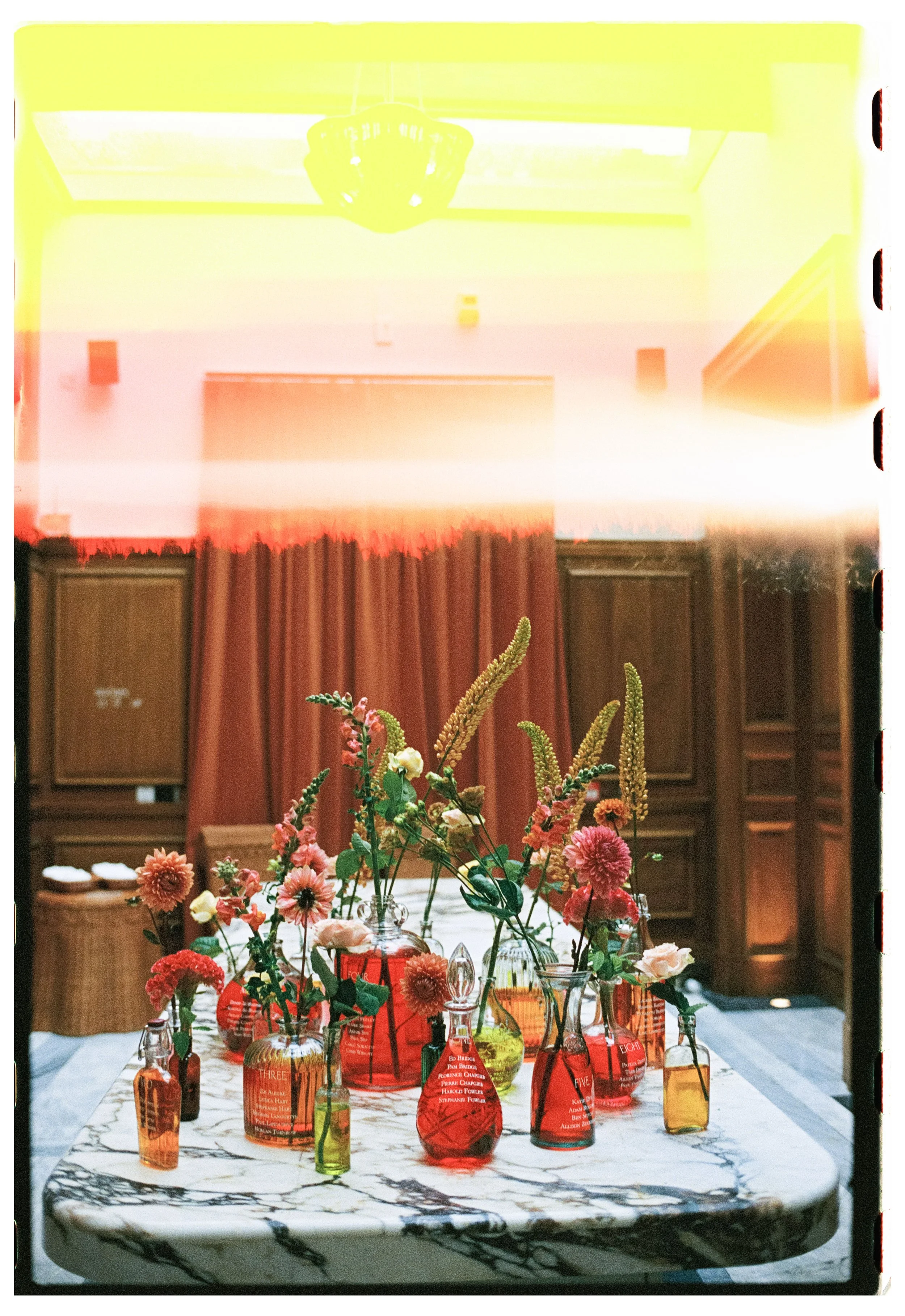 A marble table with various colorful vases and flowers, set in a wooden-paneled room with curtains.