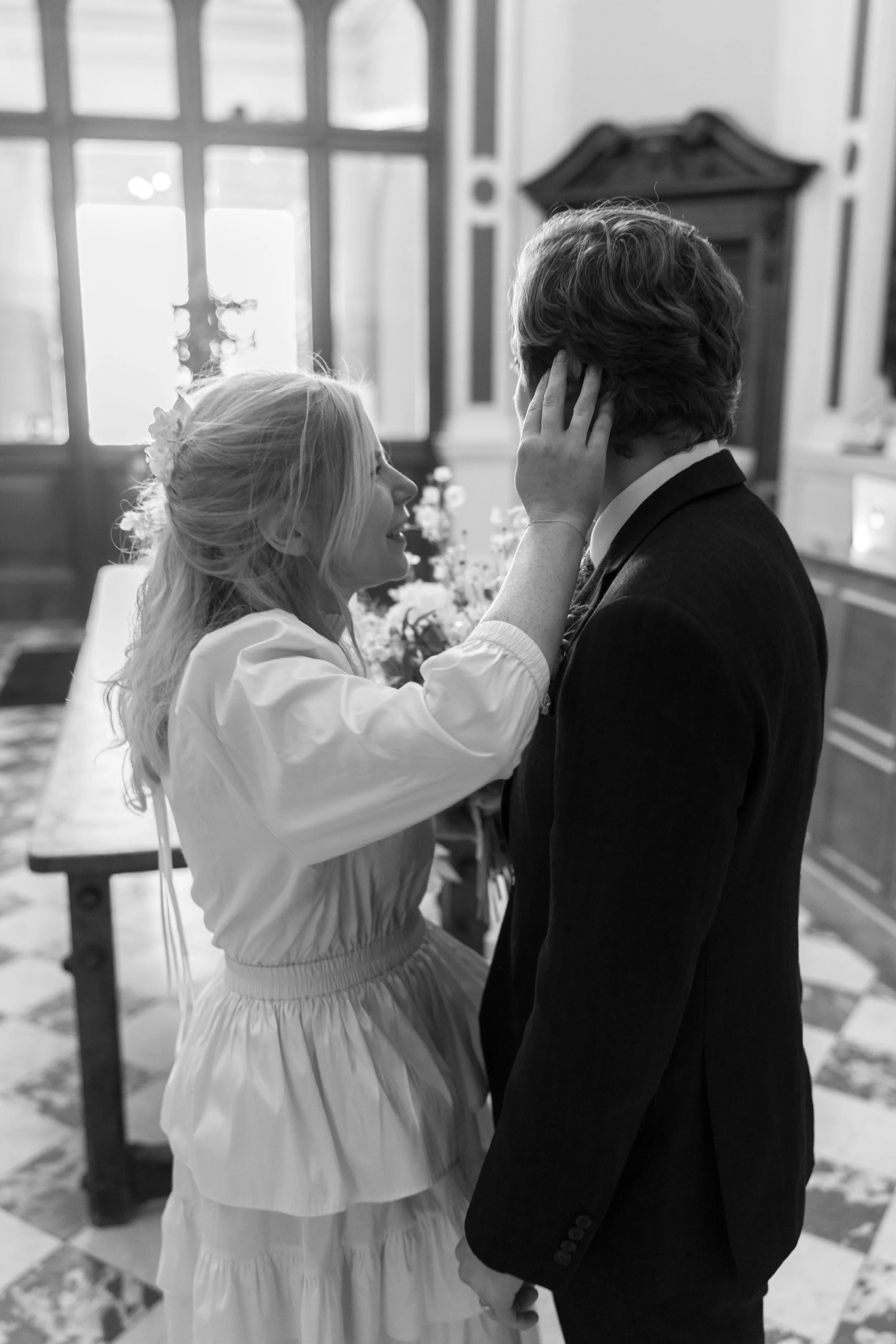 A young girl smiling and touching the face of a man in a suit, inside a room with large windows and a wooden wardrobe, black and white photograph.