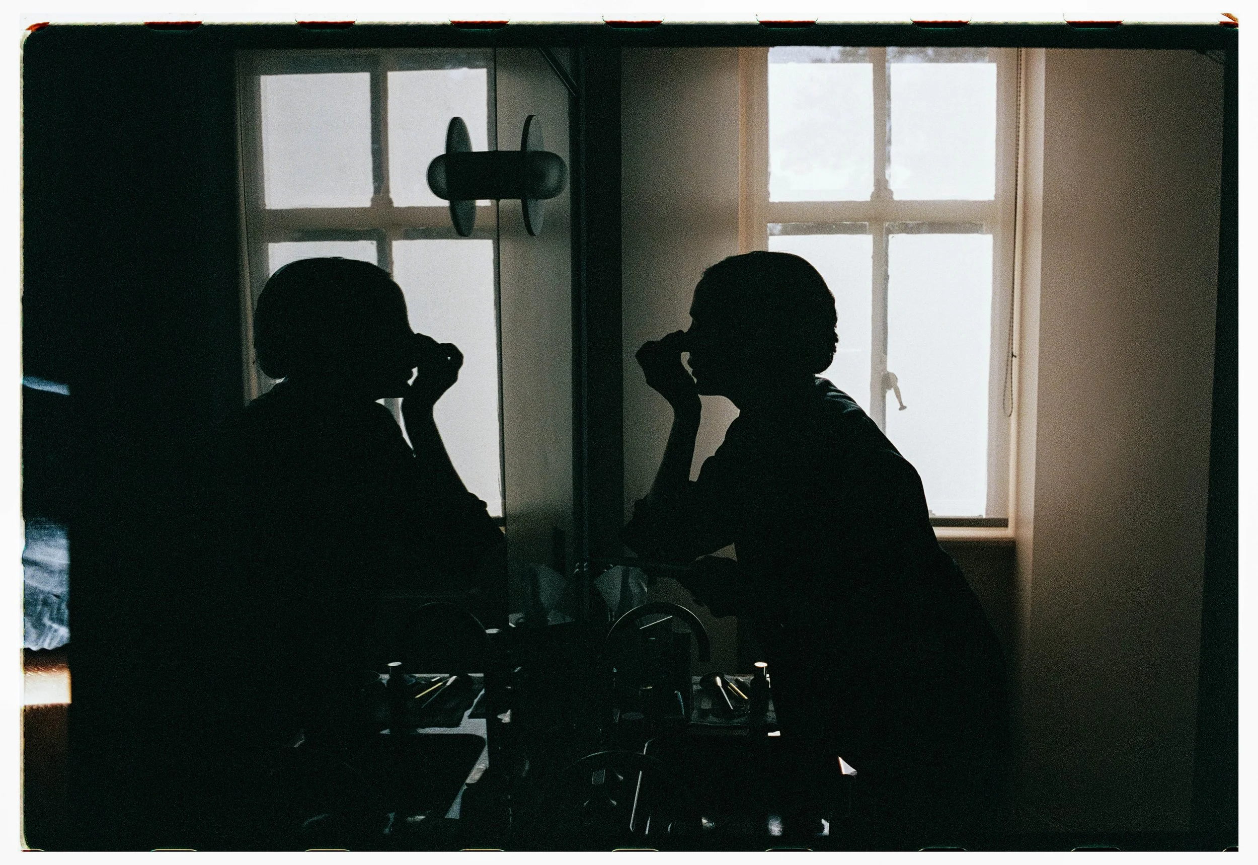 Two people sitting at a table, silhouetted against a window with frosted glass, making it difficult to see their features clearly.