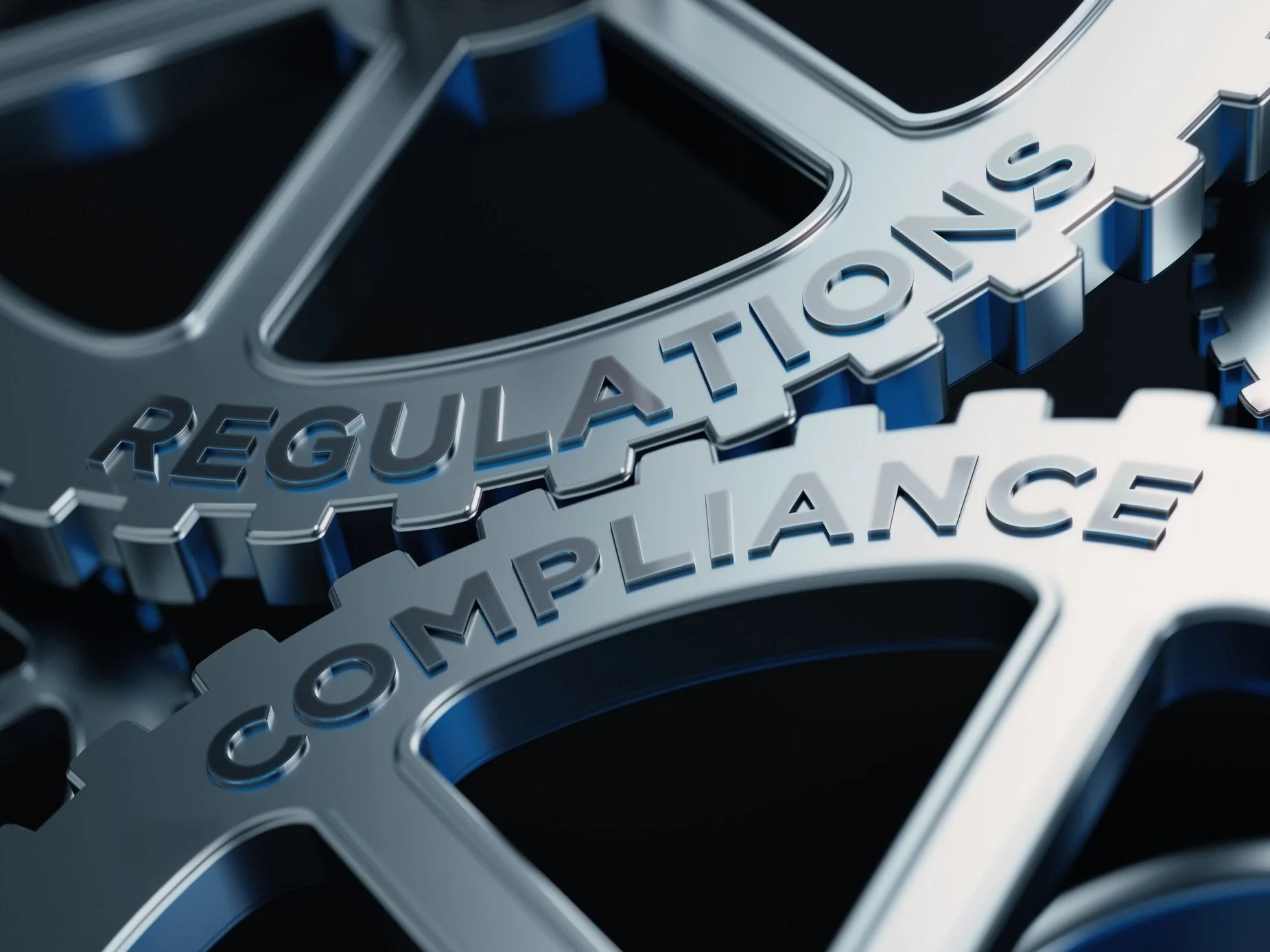 Close-up view of metallic gears engraved with the words "REGULATIONS" and "COMPLIANCE".