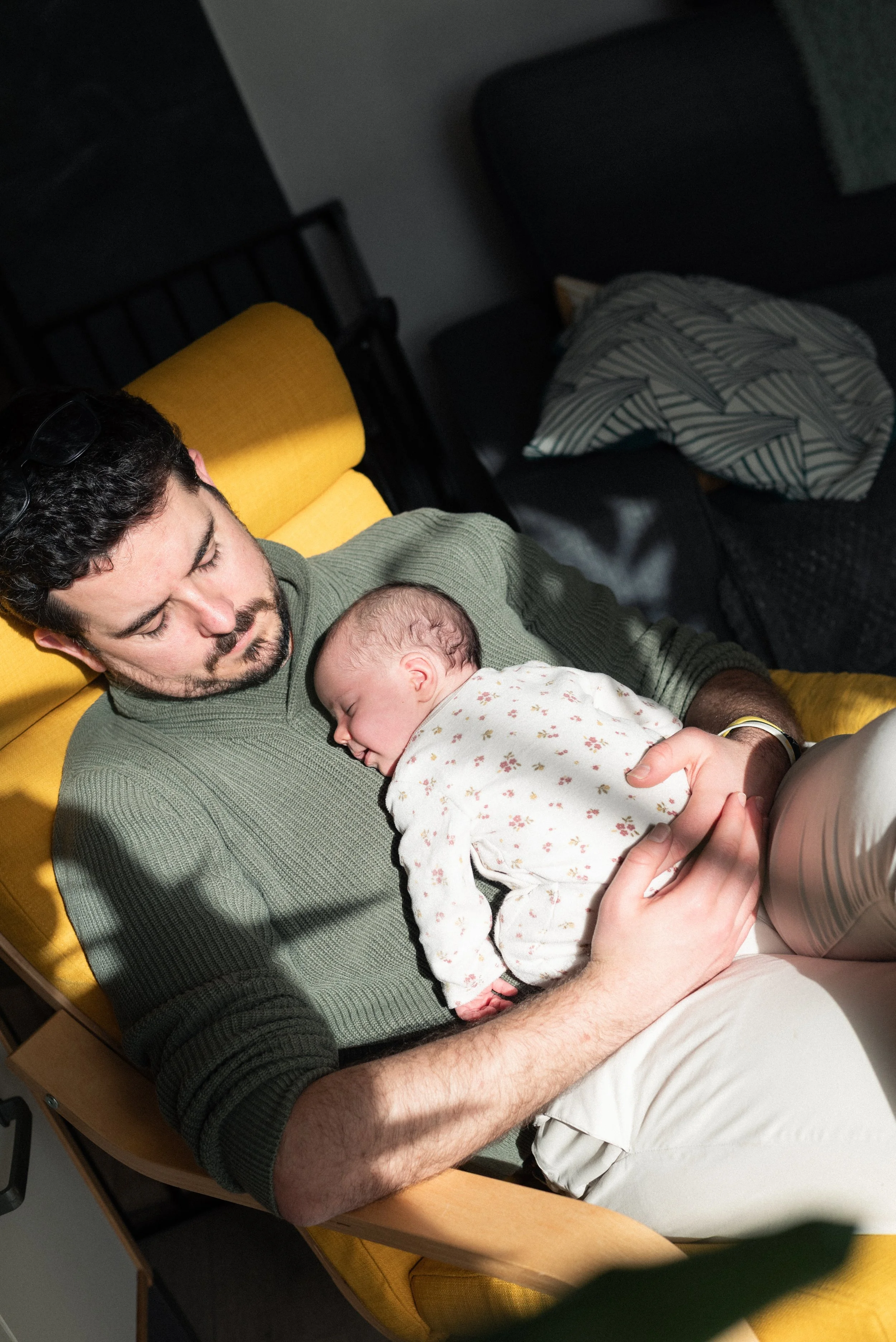 un papa dans un fauteuil jaune et son bébé sur lui dort