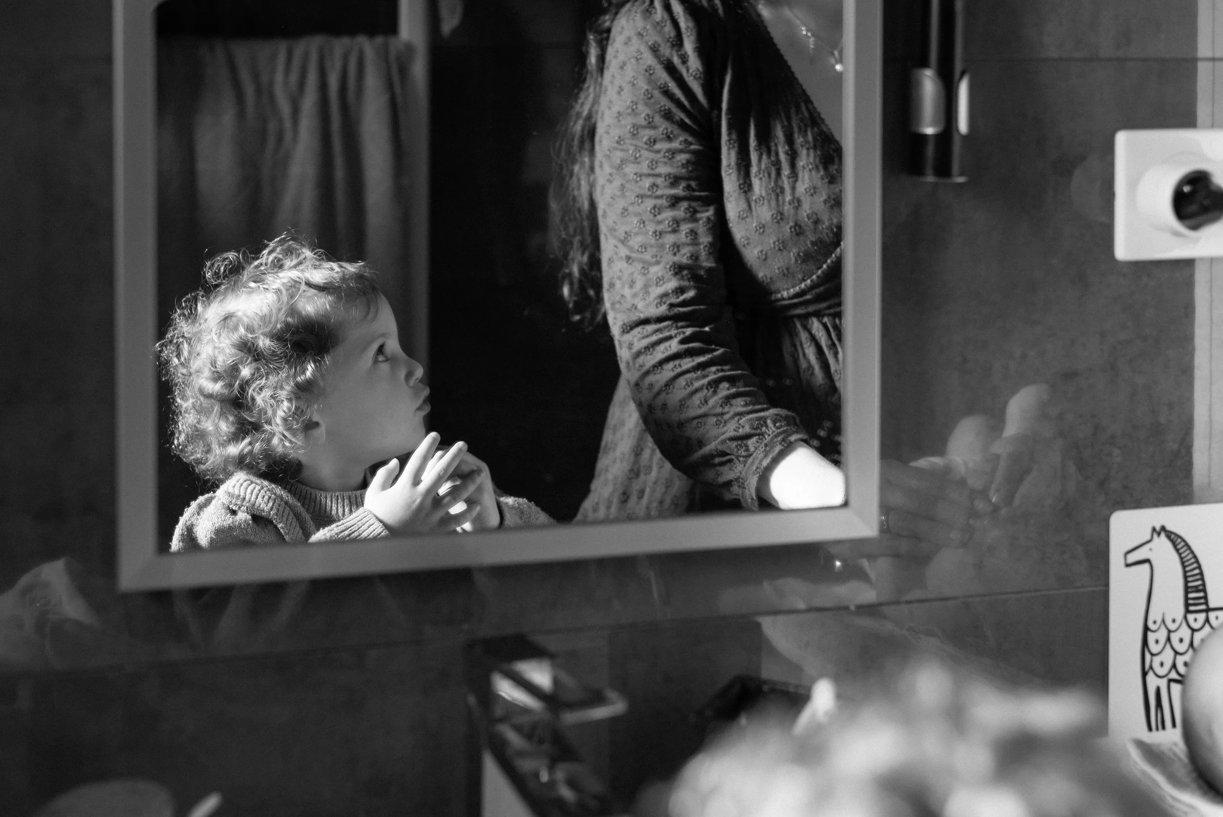 une petite fille dans le reflet du miroir de la salle de bain pendant que la maman change le bébé