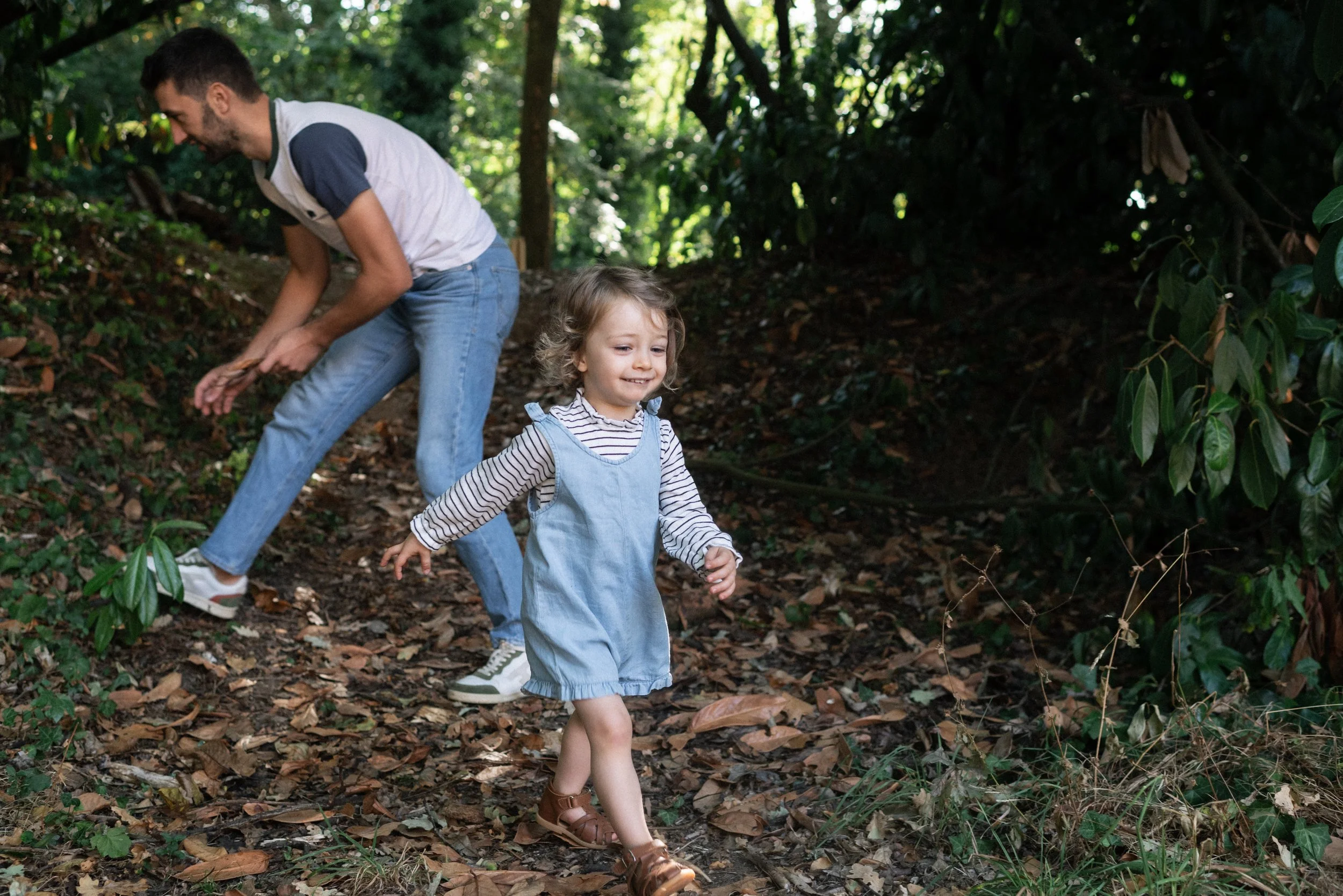 un papa cherche des feuilles pendant qu'une enfant marche