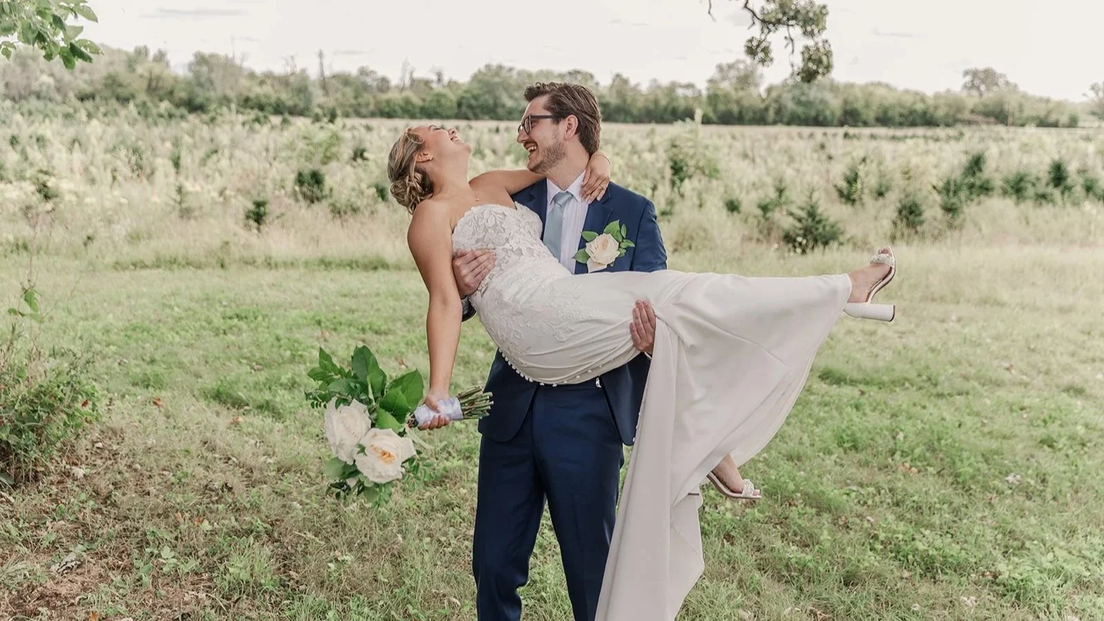 Bride laughing as groom carries her during outdoor wedding at Williams Tree Farm near Rockford, Illinois