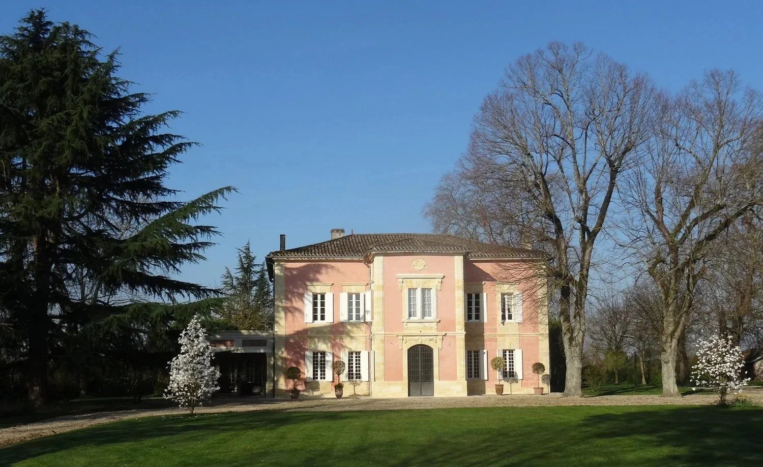 Façade rose du château des Annereaux entre de grands arbres, à Lalande-de-Pomerol