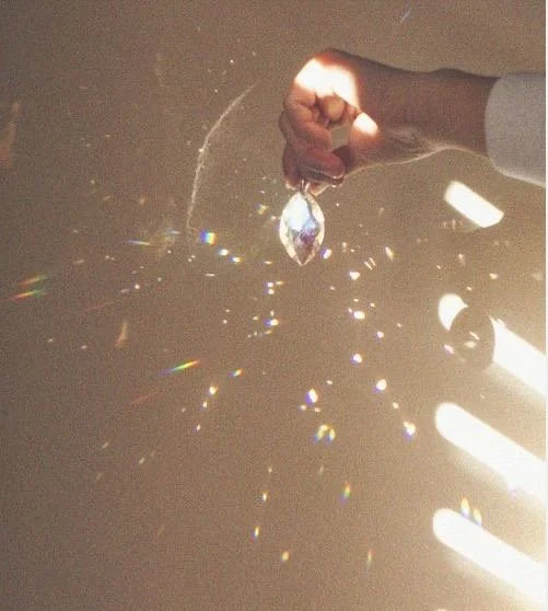 Una mano sosteniendo un colgante brillante que desprende destellos de luz y partículas en el aire.