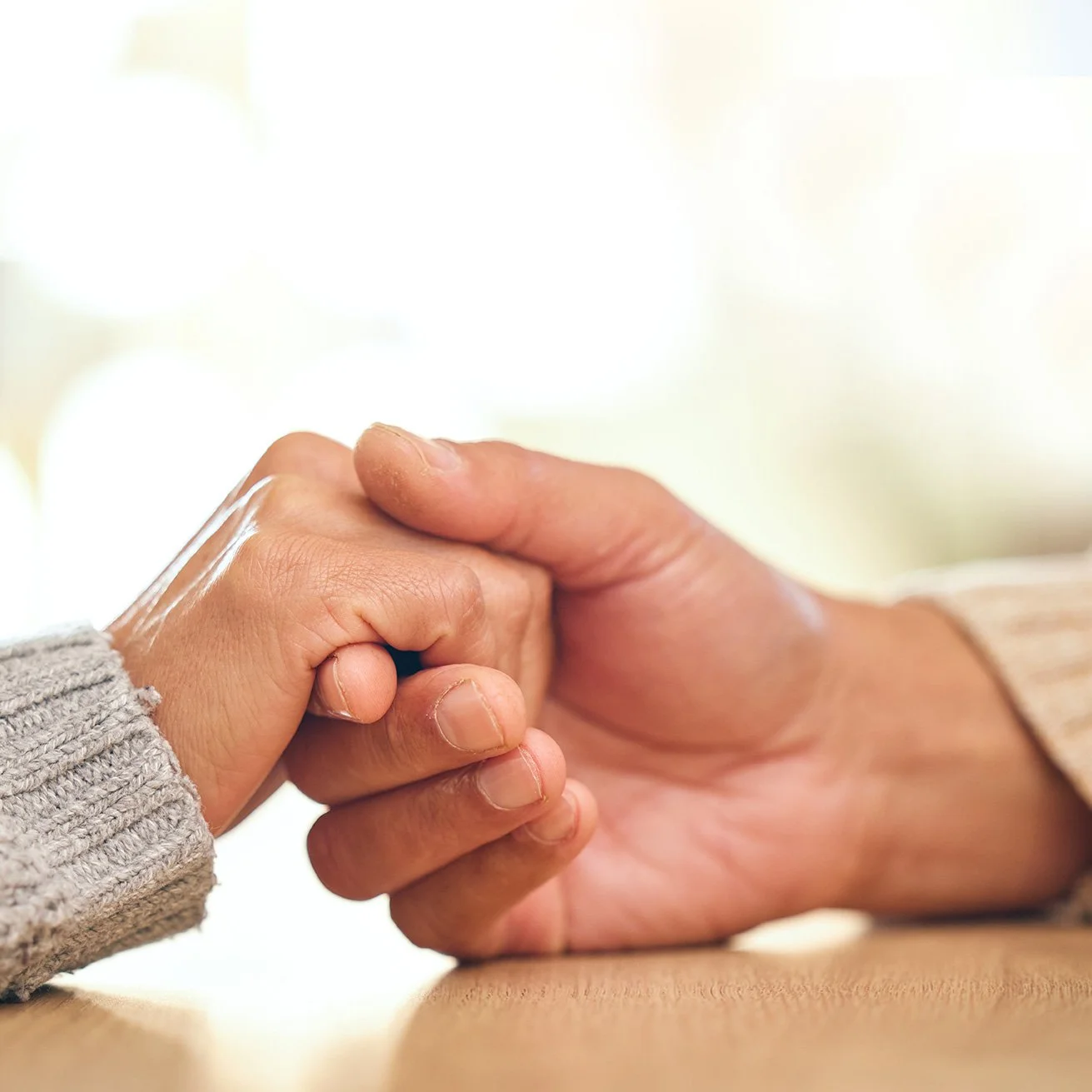 Two hands holding each other, one adult and one child, with a blurred light background.