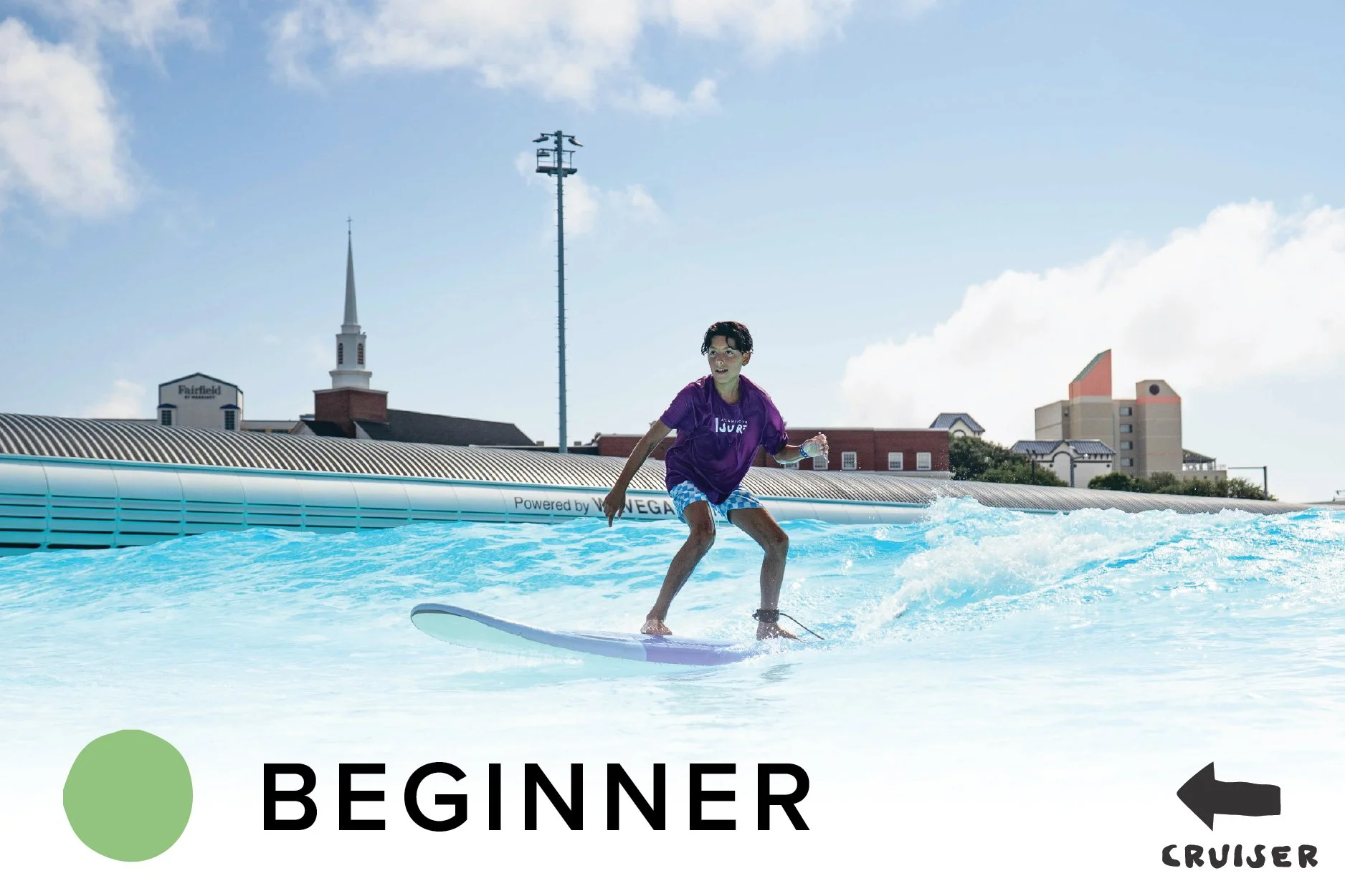 A person surfing on a wave at an outdoor artificial water park with city buildings in the background.