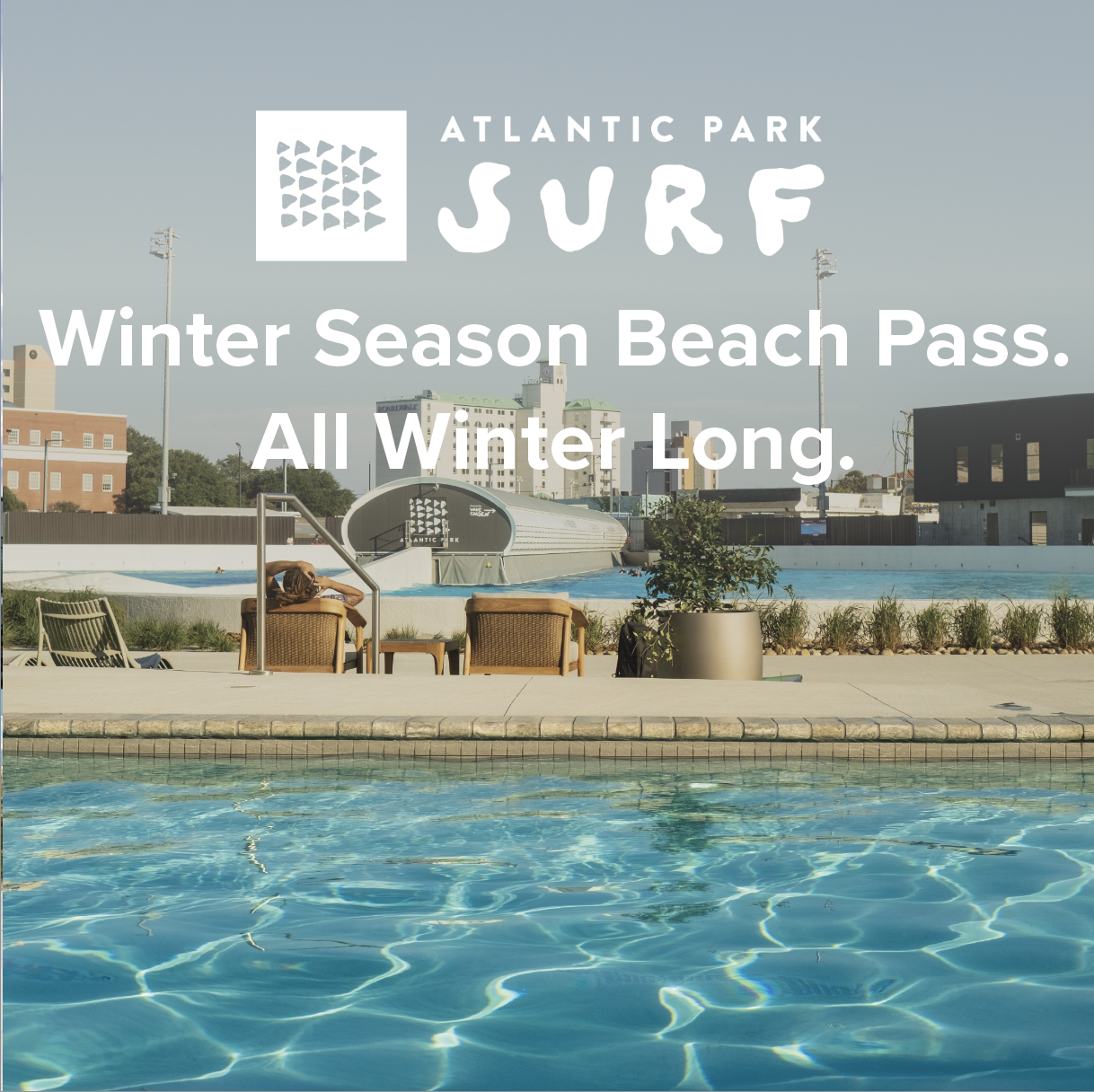 A person relaxing on a poolside chair at Atlantic Park surf, with a swimming pool in the foreground and city buildings in the background, promoting a winter season beach pass.