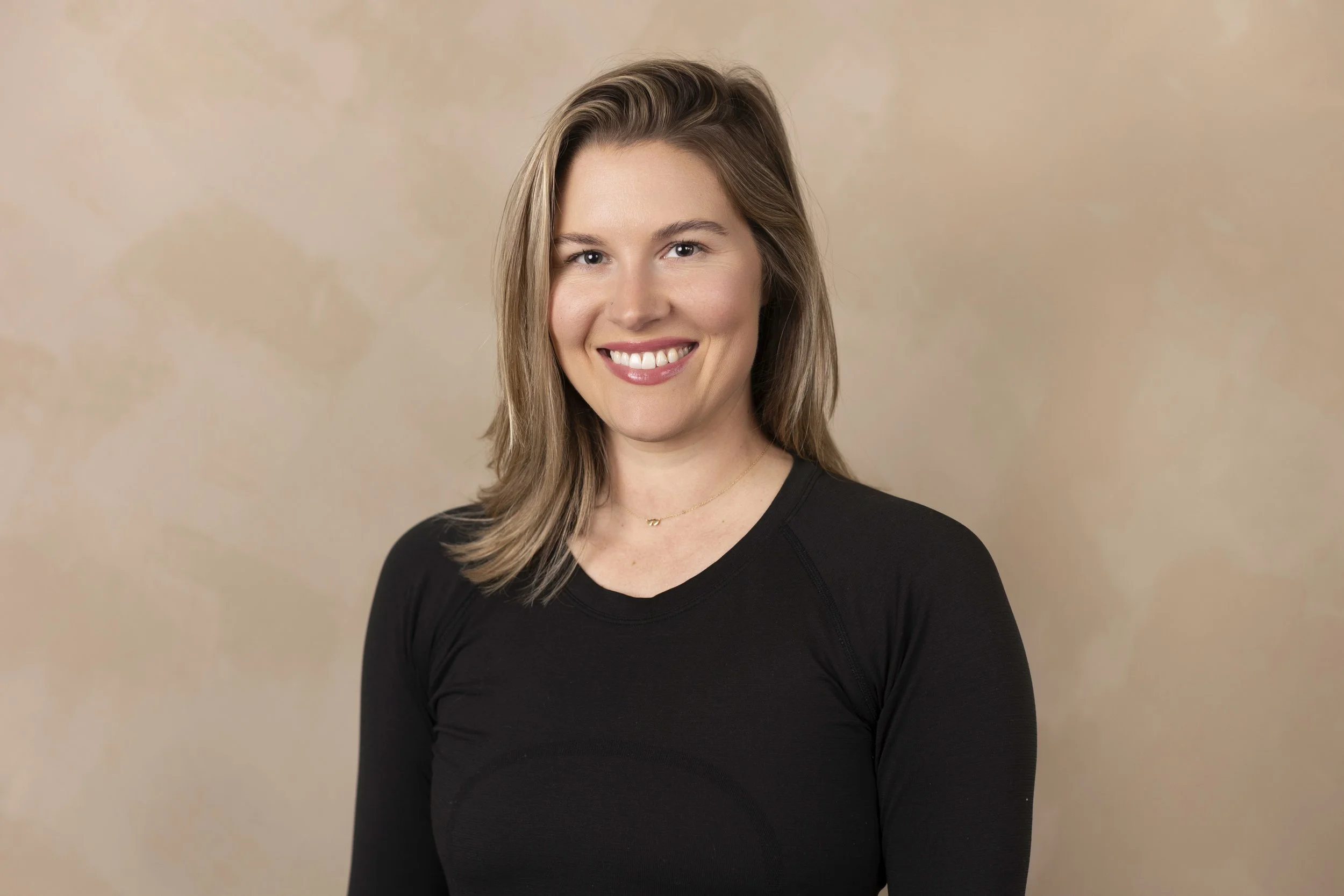 portrait of a smiling woman with shoulder-length light brown hair wearing a black top against a beige background