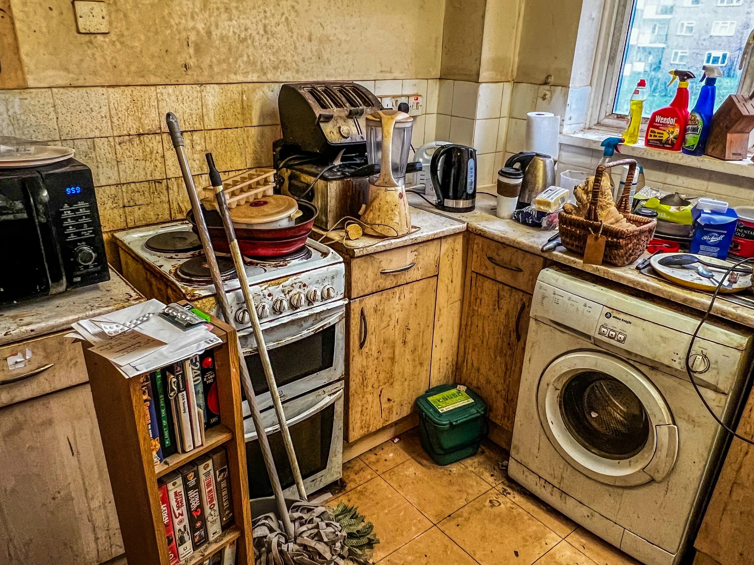 Cluttered and messy kitchen with appliances, dishes, and cleaning supplies.