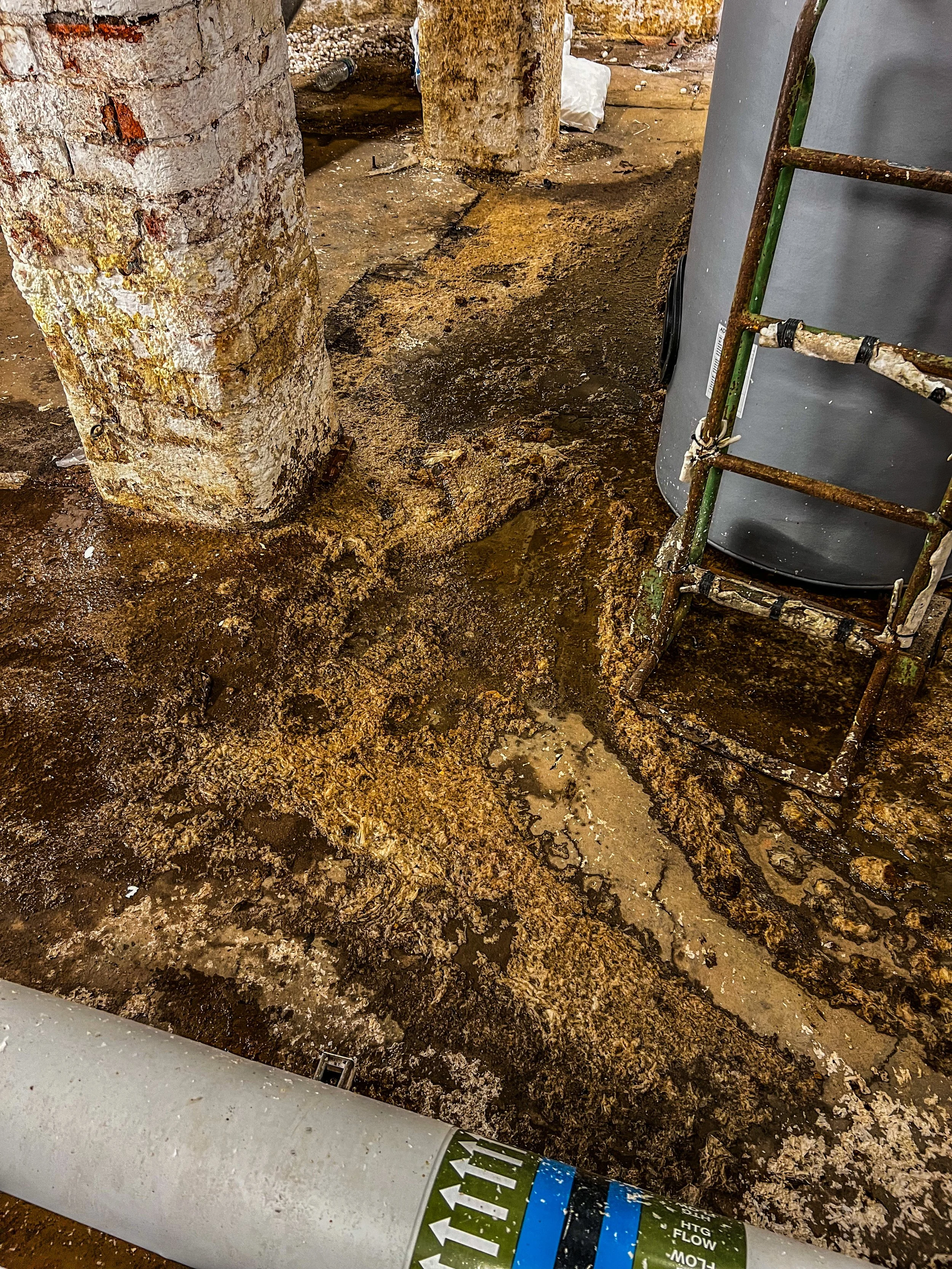 Industrial space with rusted metal beams, concrete pillars, and exposed pipes in a gritty environment.