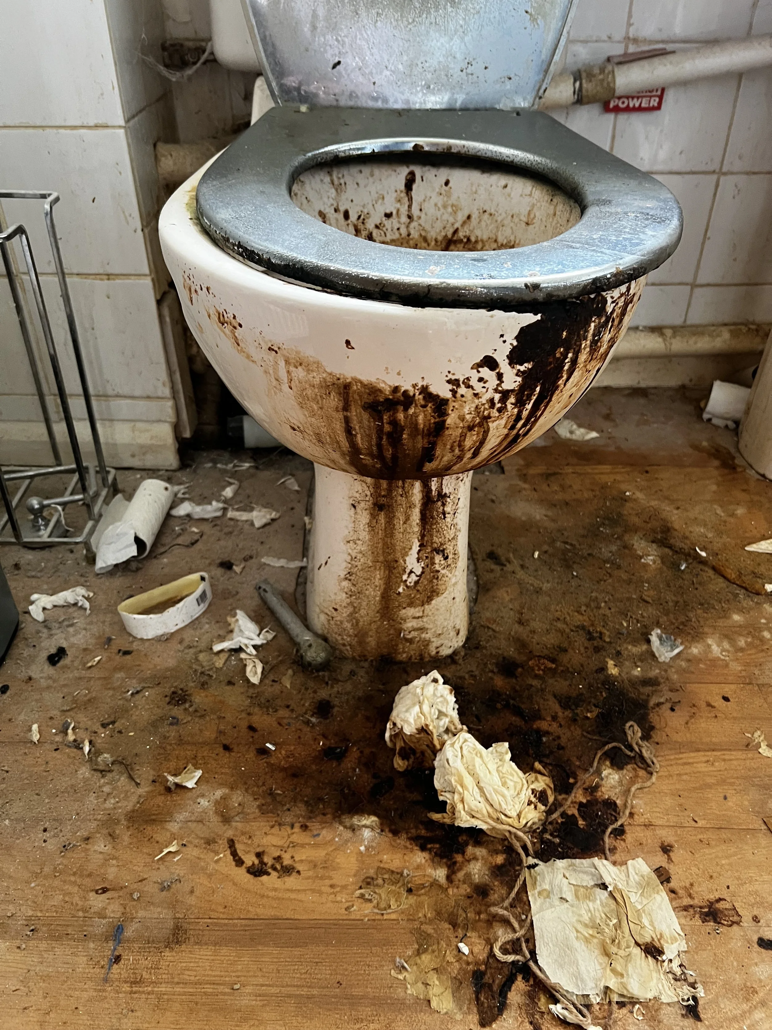 Dirty and stained toilet with surrounding mess on the floor.