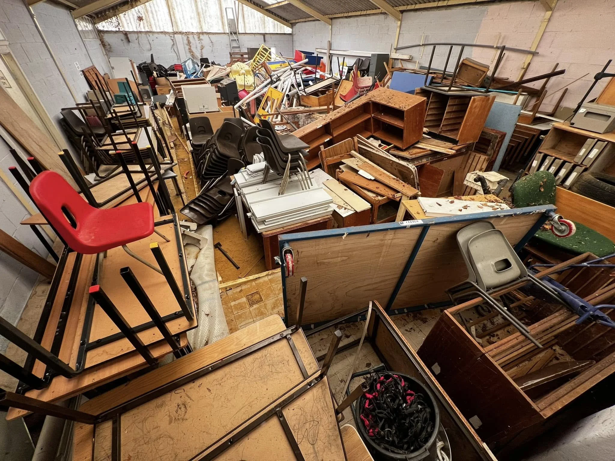 Cluttered storage space filled with stacked chairs, tables, and assorted furniture.
