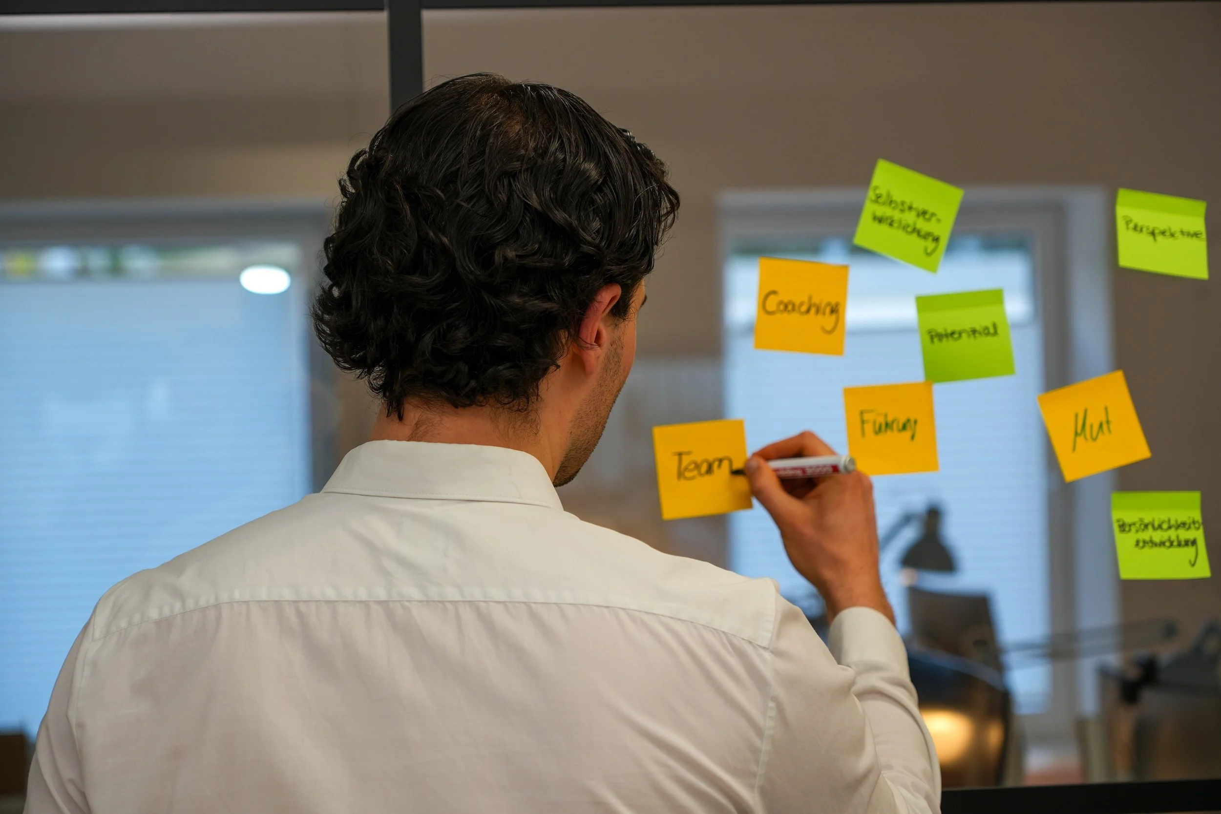 Marco Schmitt steht an einer Glaswand und beschriftet Post-Its
