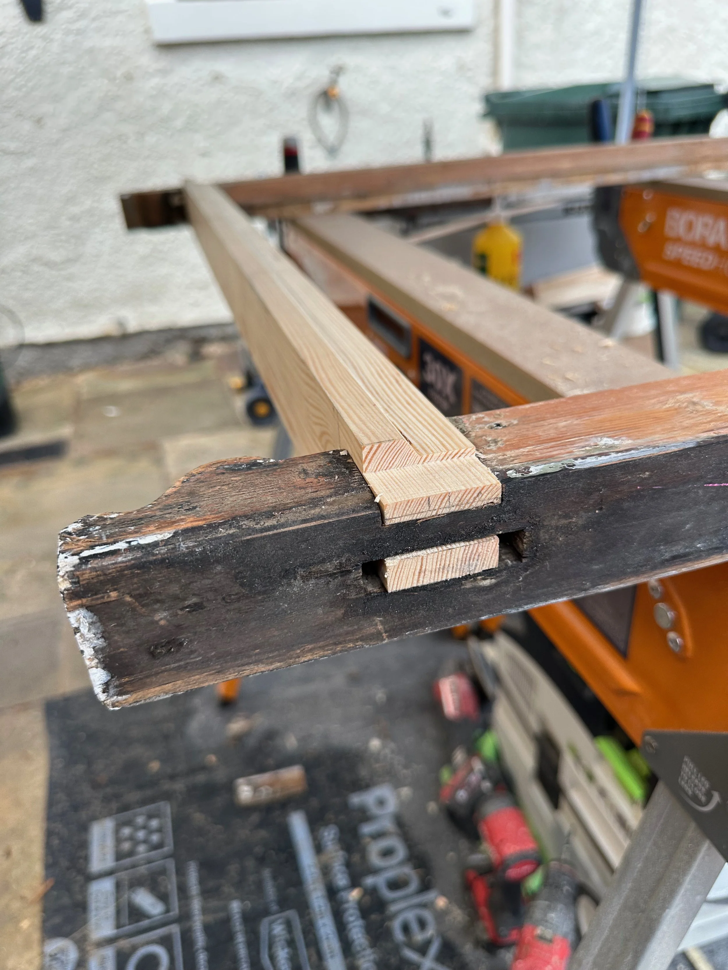 A woodworking workspace with a worn wooden plank and a freshly cut piece of lumber on a workbench, with tools and equipment in the background.