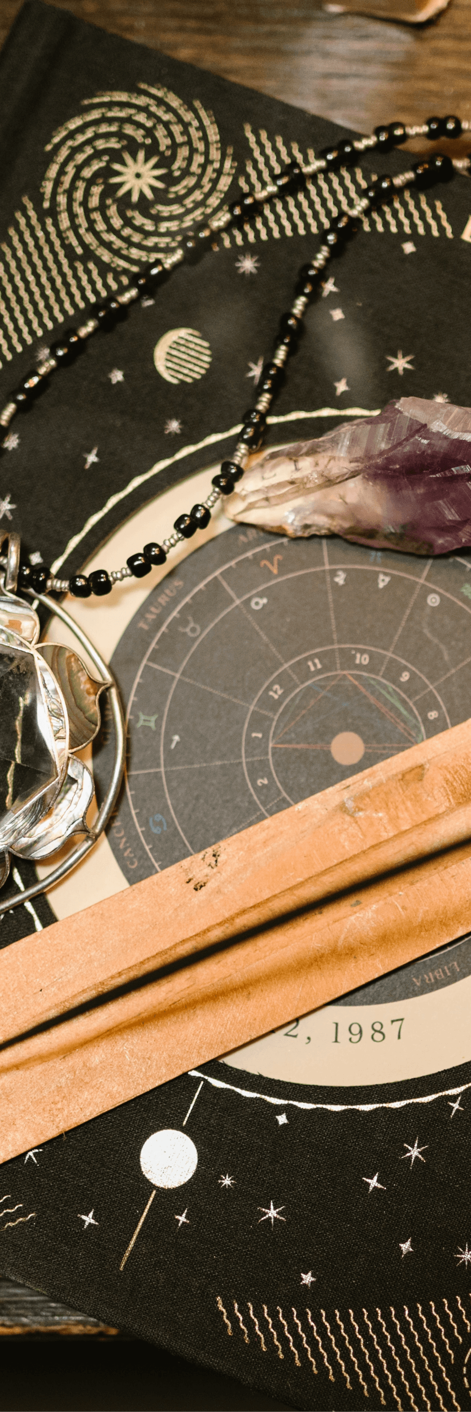 A lunar calendar, a crystal, a beaded necklace, and a wooden stick on a star-themed cloth.