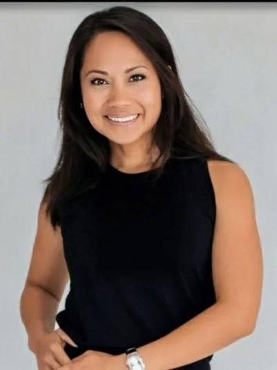 Smiling woman with dark hair in a sleeveless black top, posing against a plain light background.