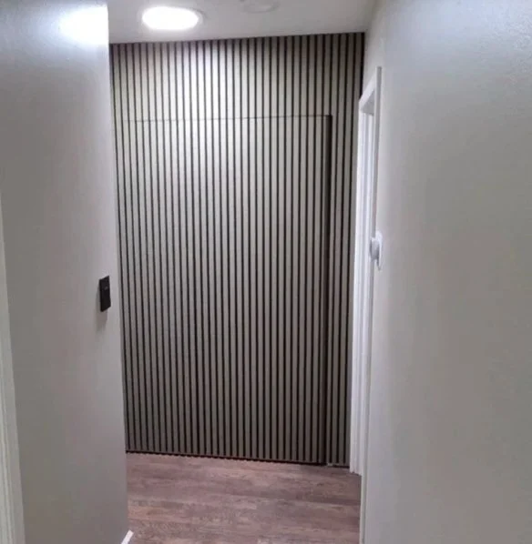 Floor-to-ceiling vertical slat feature wall with dark wood finish in hallway, hiding closet