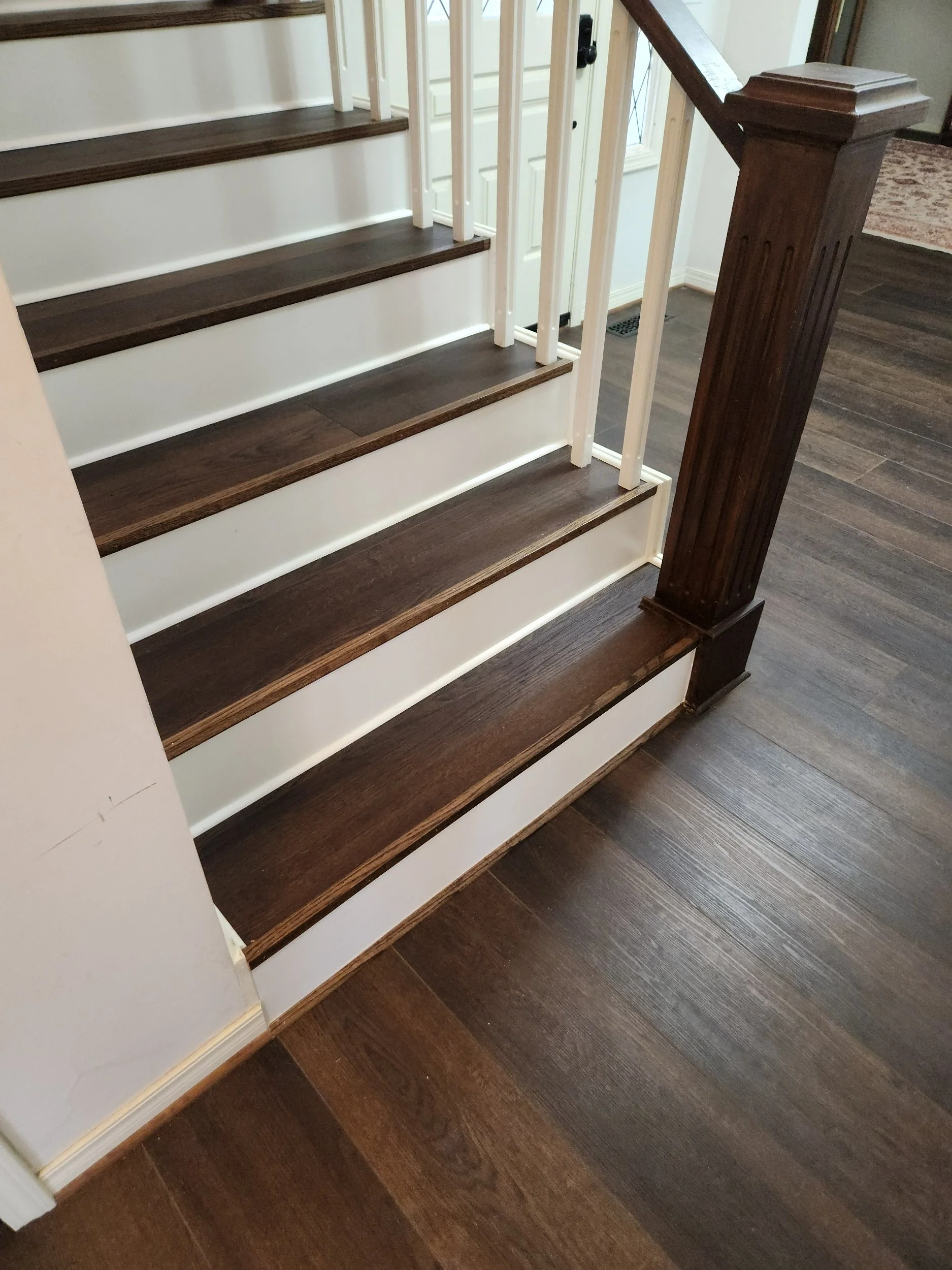 Finished staircase with luxury vinyl flooring and stained hardwood trim