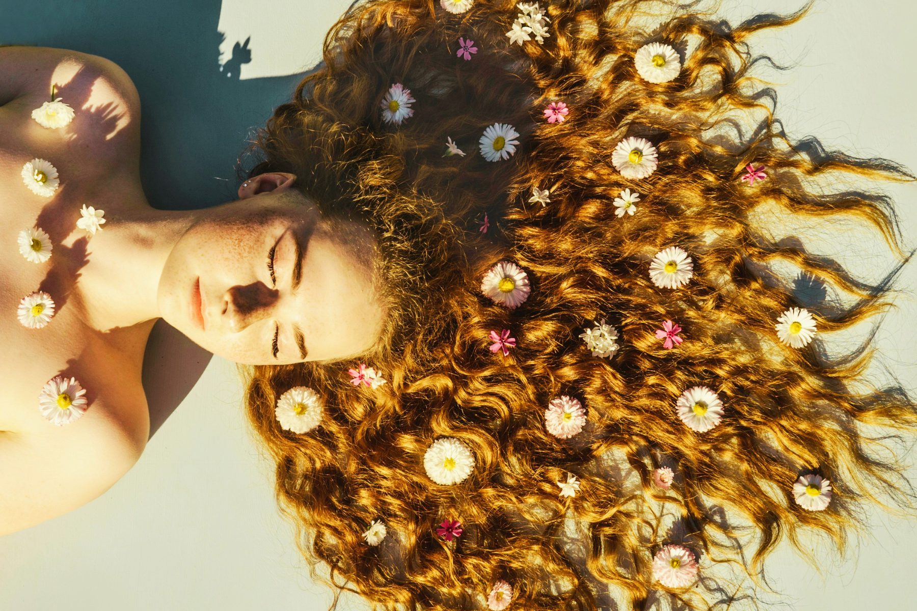 Woman with curly orange hair laying on ground with flowers sprinkled throughout