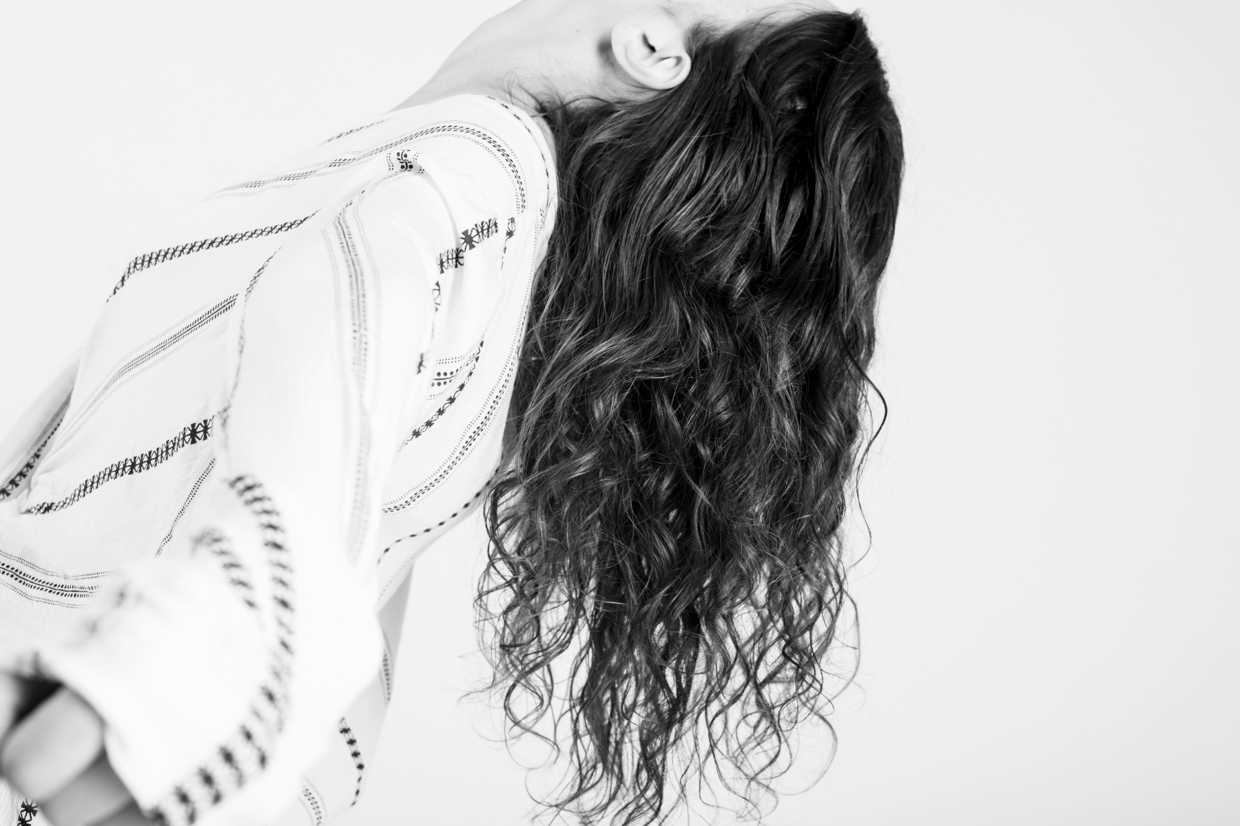 black-and-white-photo-of-woman-leaning-backwards-with-curly-hair-on-white-background