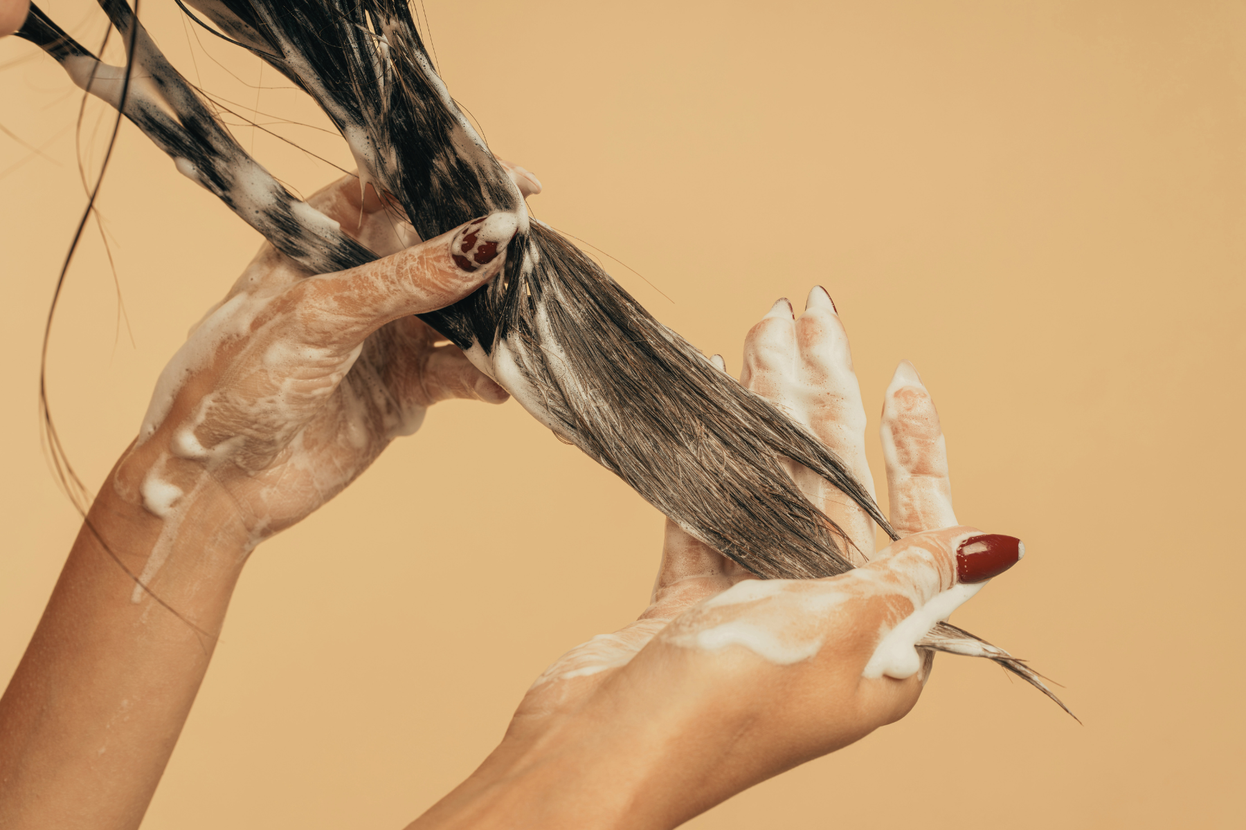 Woman running conditioner through hair strands on gold background