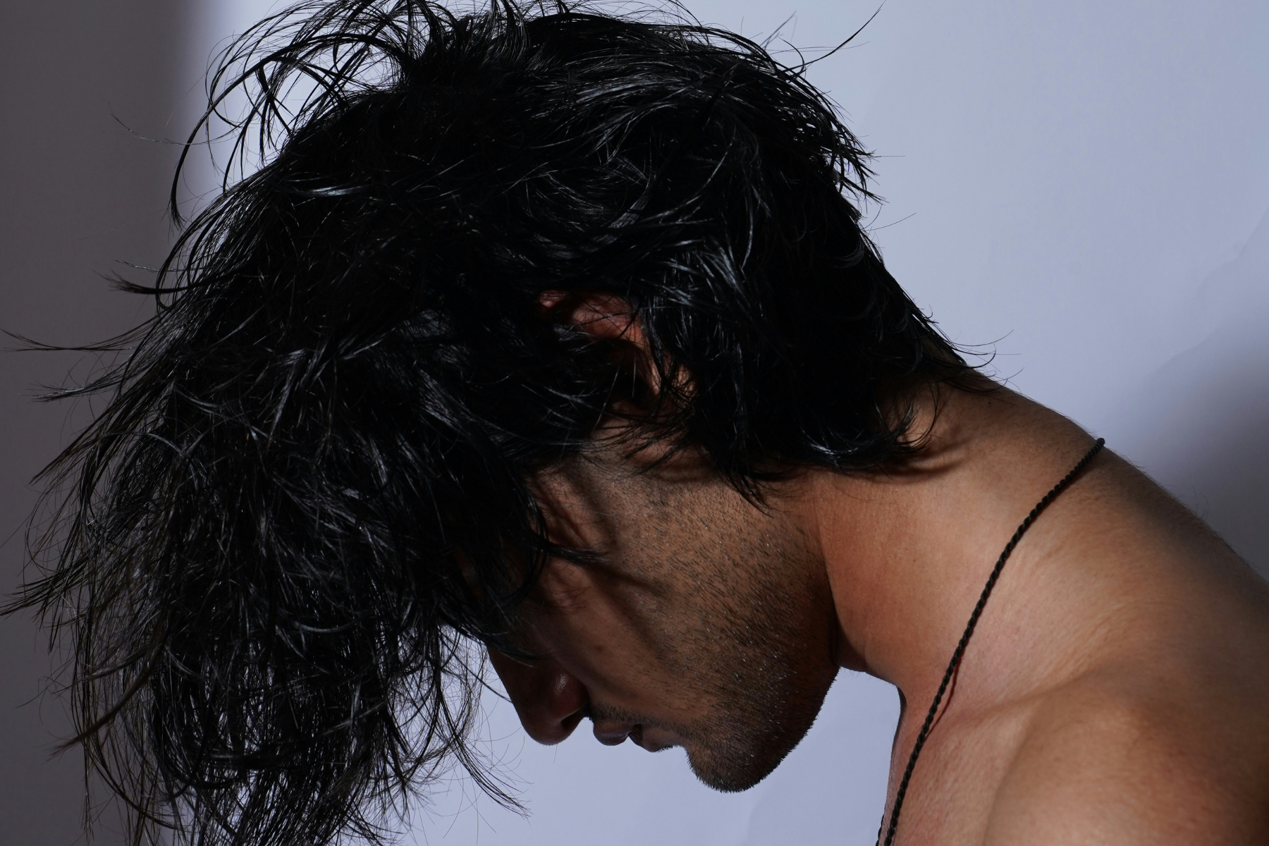 Man with flowing hair facing down against a white background