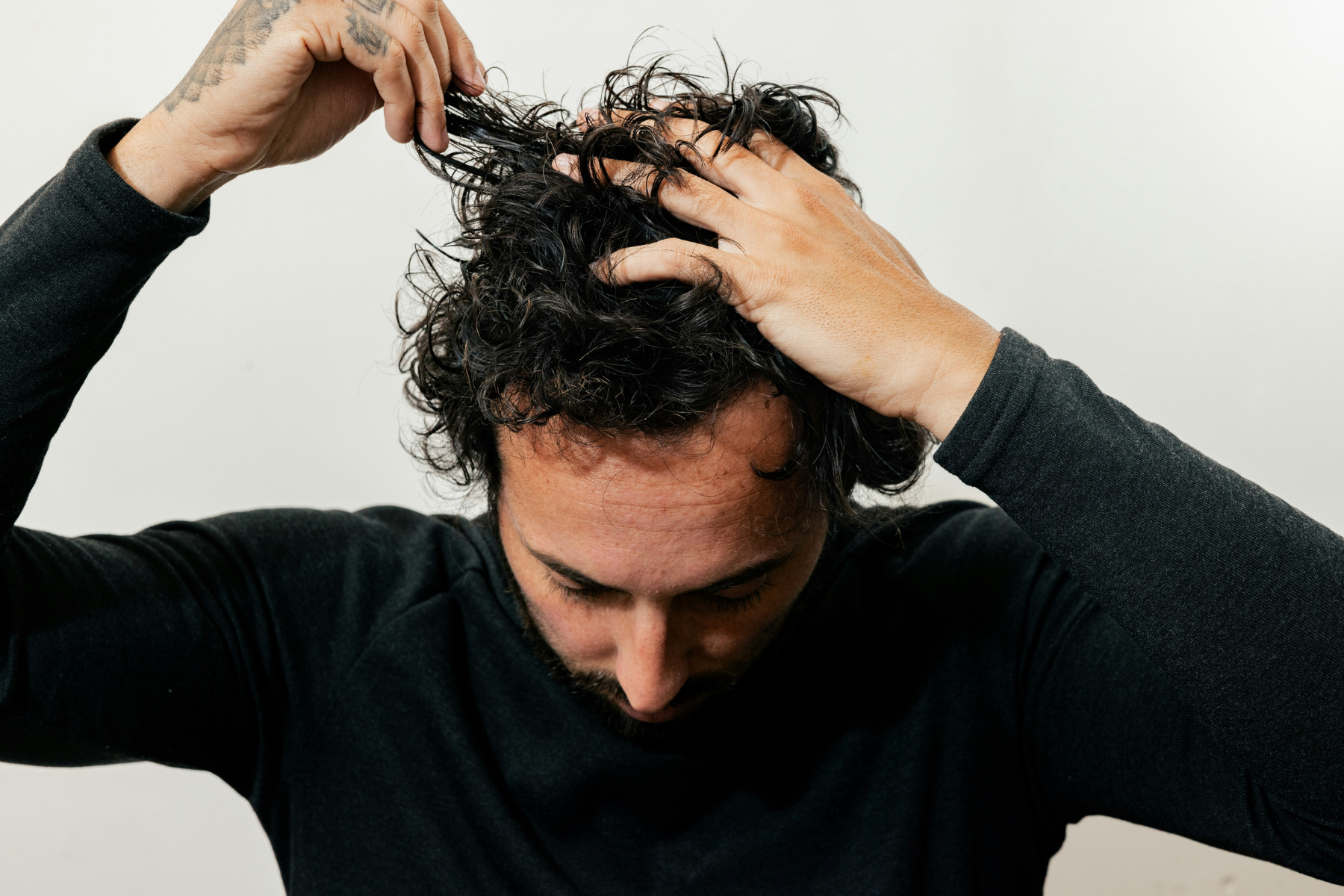 Men leaning forward against white background holding his dark curly hair