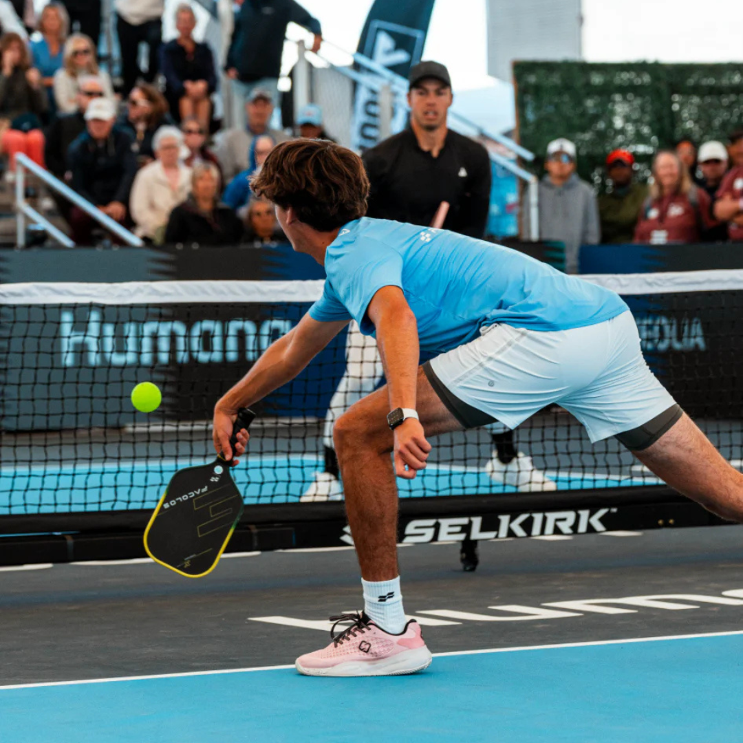 Close-up of a person's foot wearing a bright blue athletic sneaker with white laces, paired with a white sock and black pants, on a concrete surface near stairs.
