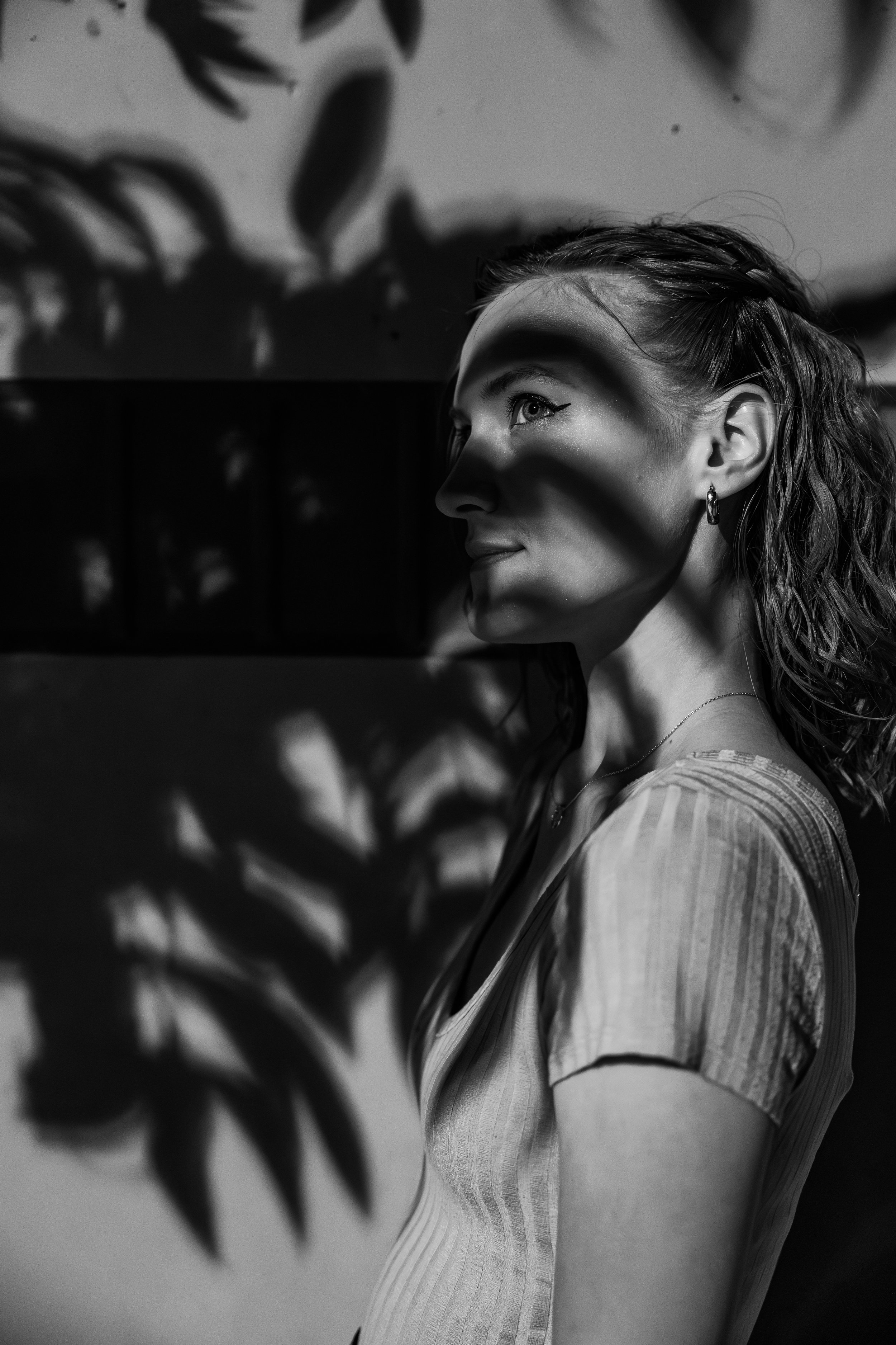 A black-and-white photo of a woman in profile with light casting shadows across her face, background includes shadows of leaves.