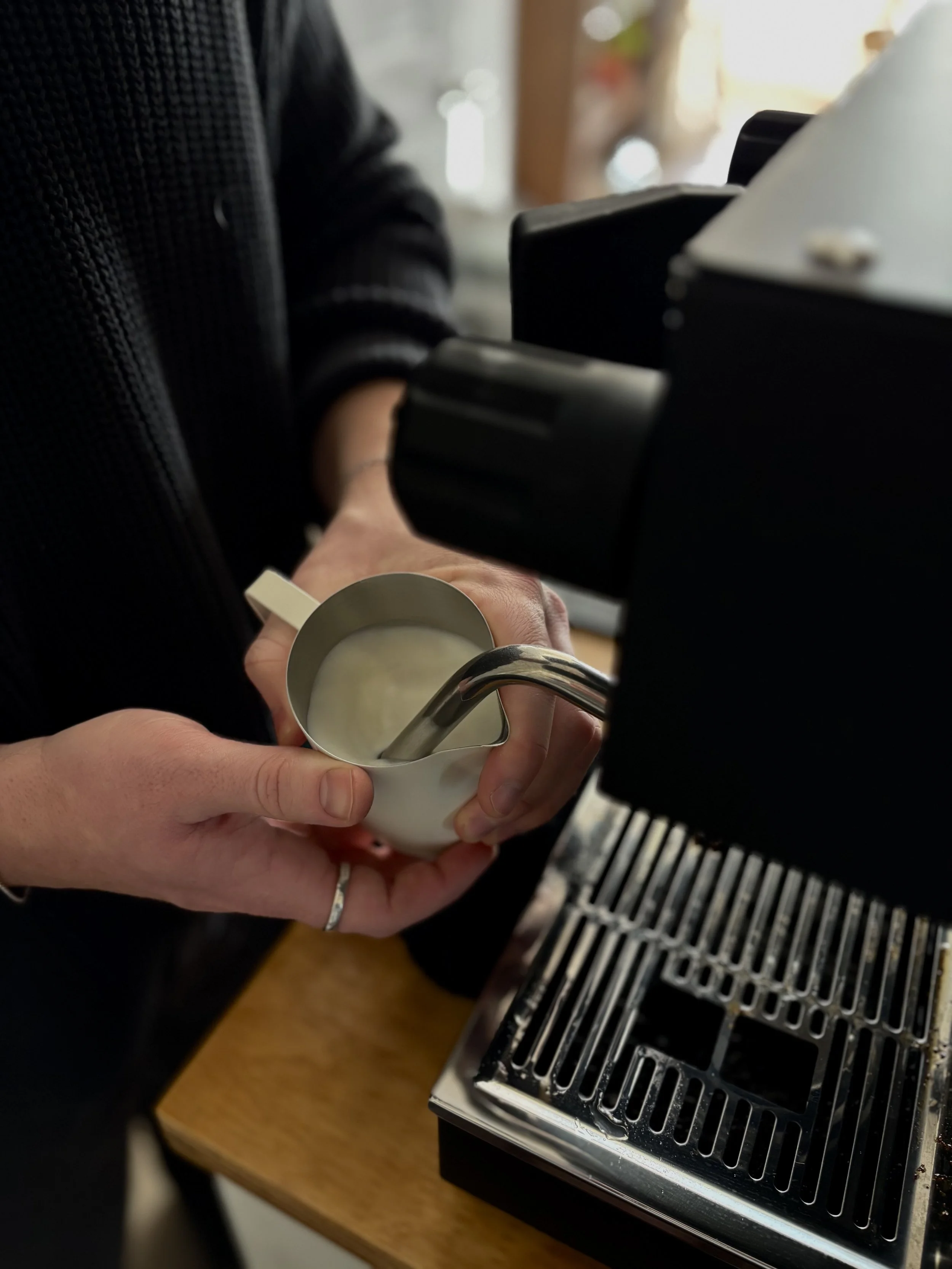 Eden & Oak Mobile Coffee Cart barista steaming milk using a professional espresso machine, with hands holding a metal pitcher and a white cup under the steam wand.