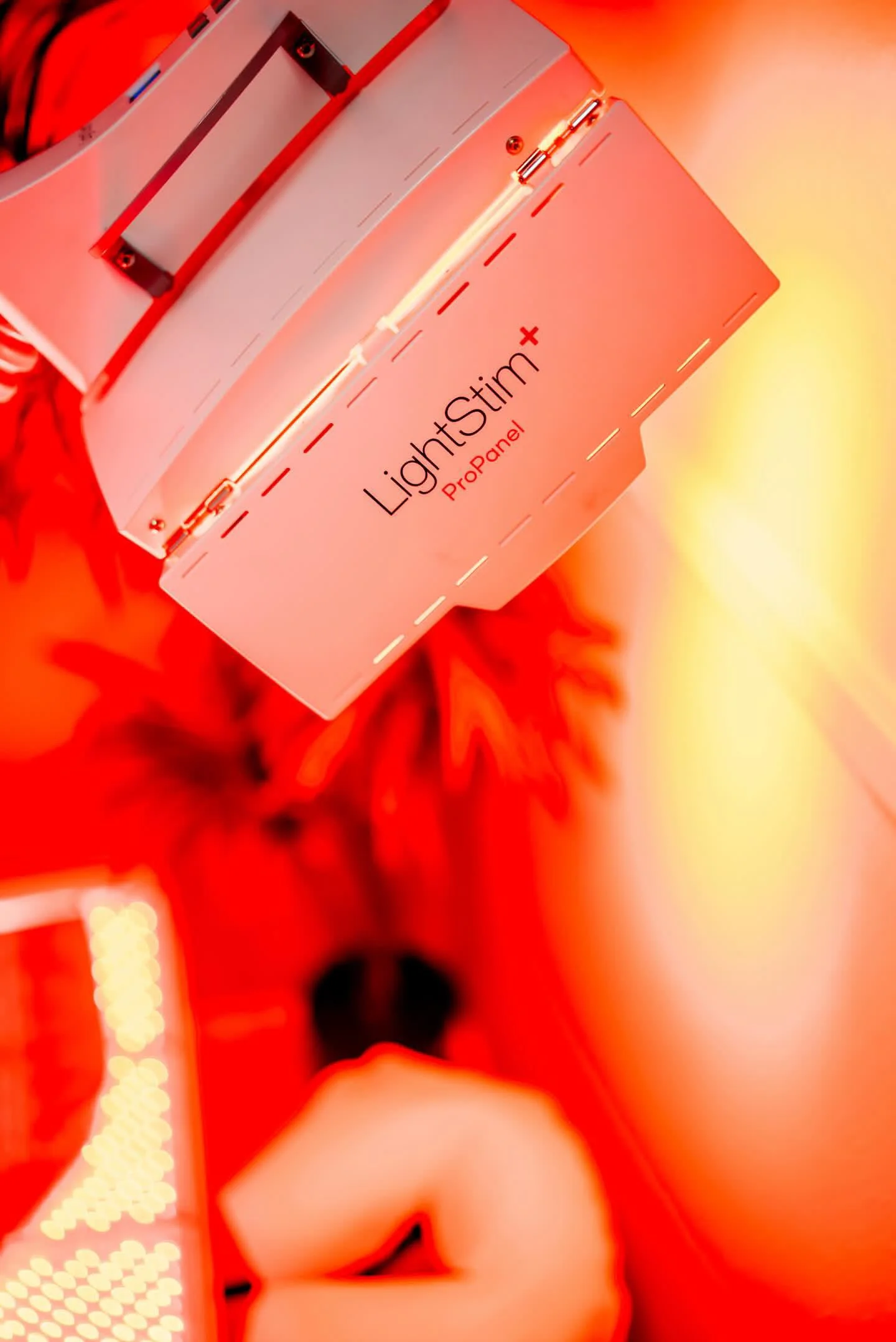 A device labeled LightStim+ ProPanel emitting red light, held by a person in a room illuminated with red light.