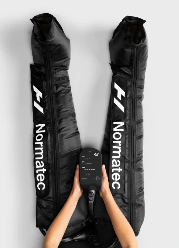 Two black padded sports gear bags with white text reading "Normaltec" and a person holding a small black device with a screen and buttons between the bags.