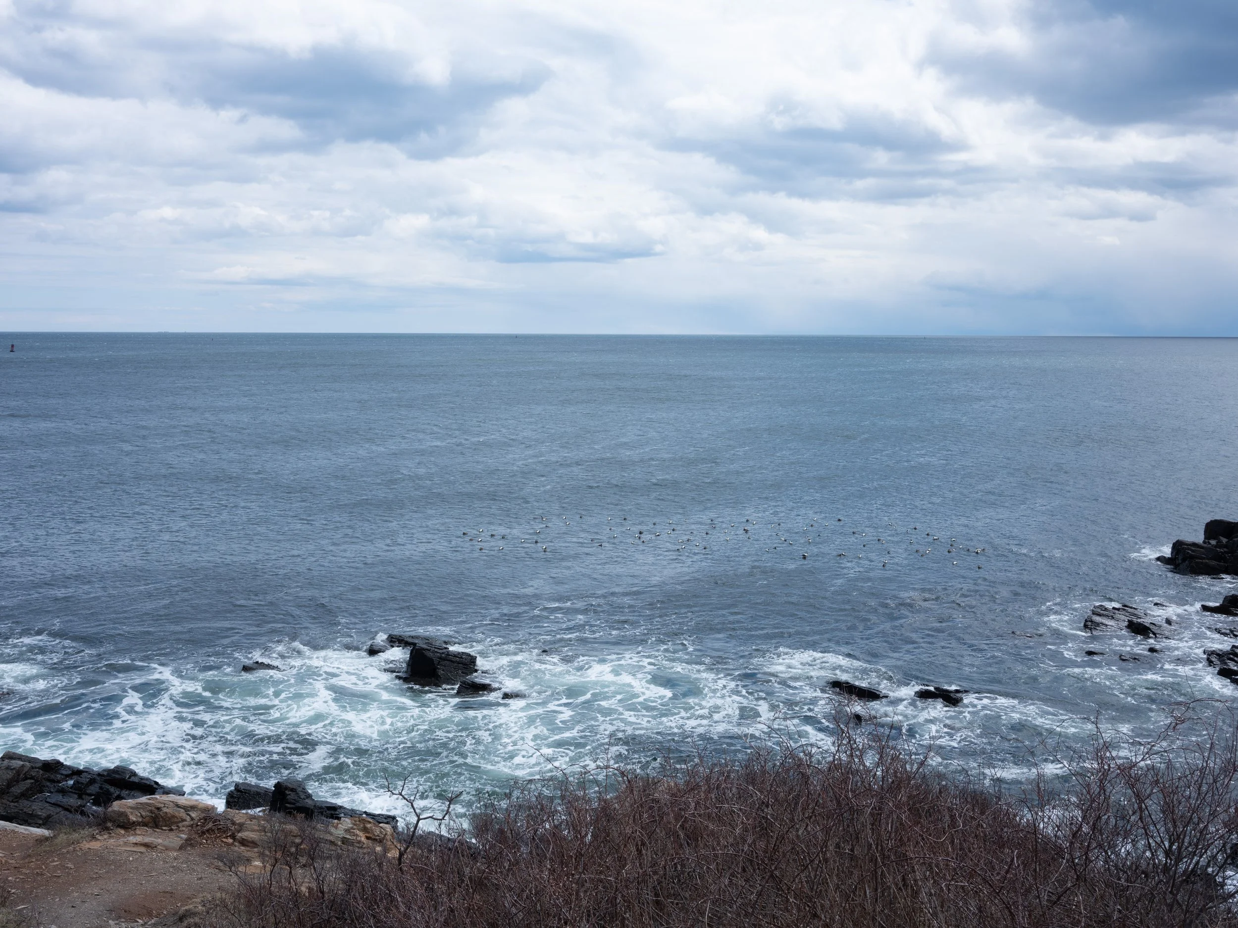 Overcast sky over the ocean with rocks and waves in the foreground.