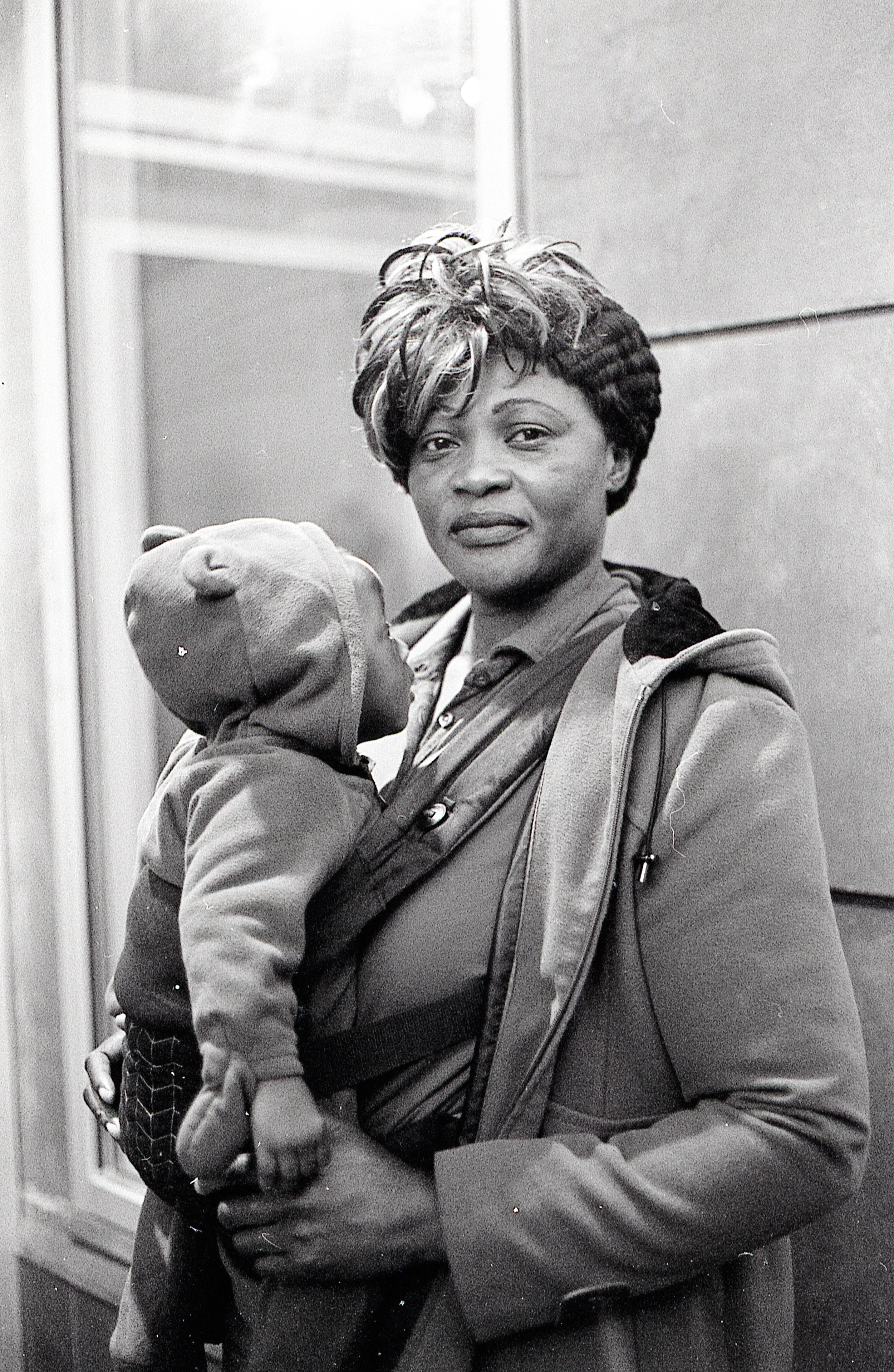 A woman holding a sleeping child in a baby carrier outside a building.