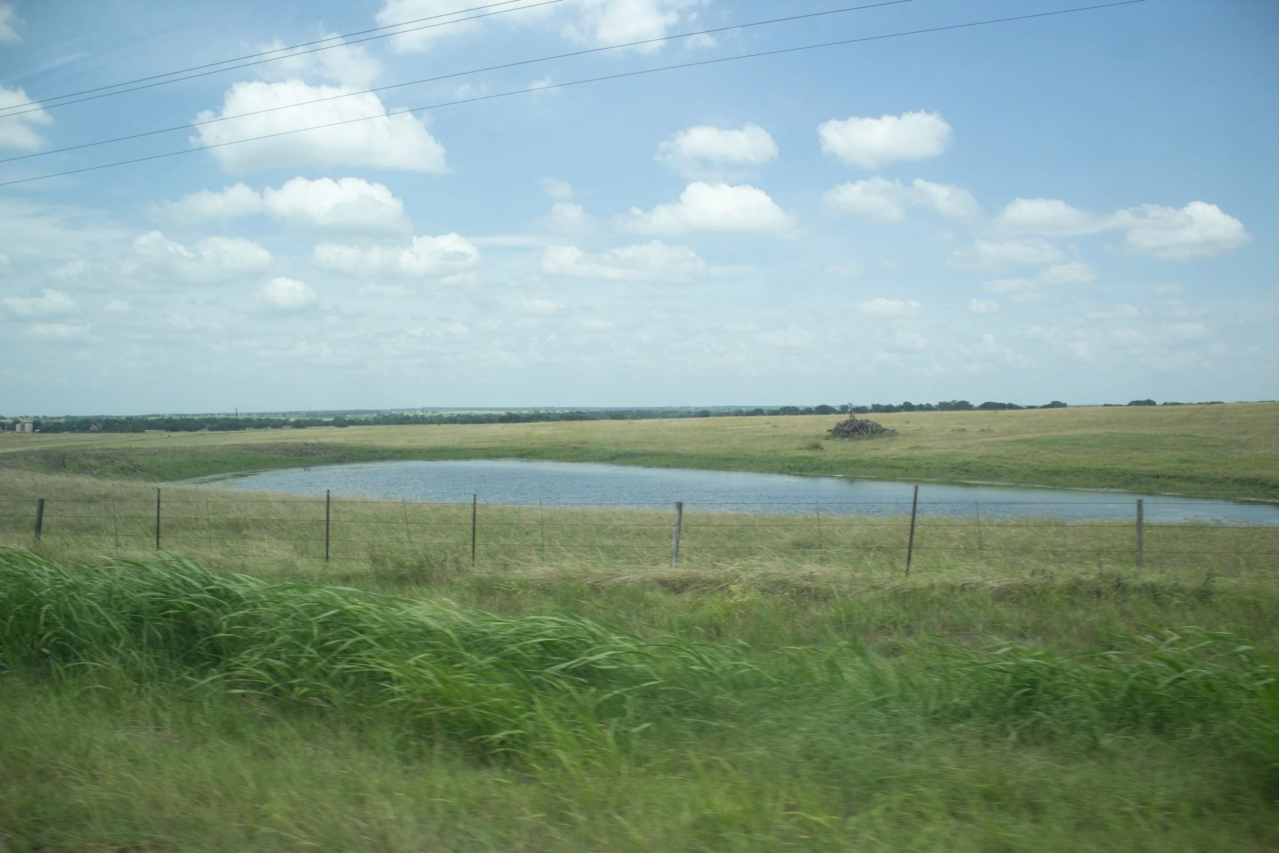 Scenic view of a grassy field with a small pond and a cloudy blue sky.