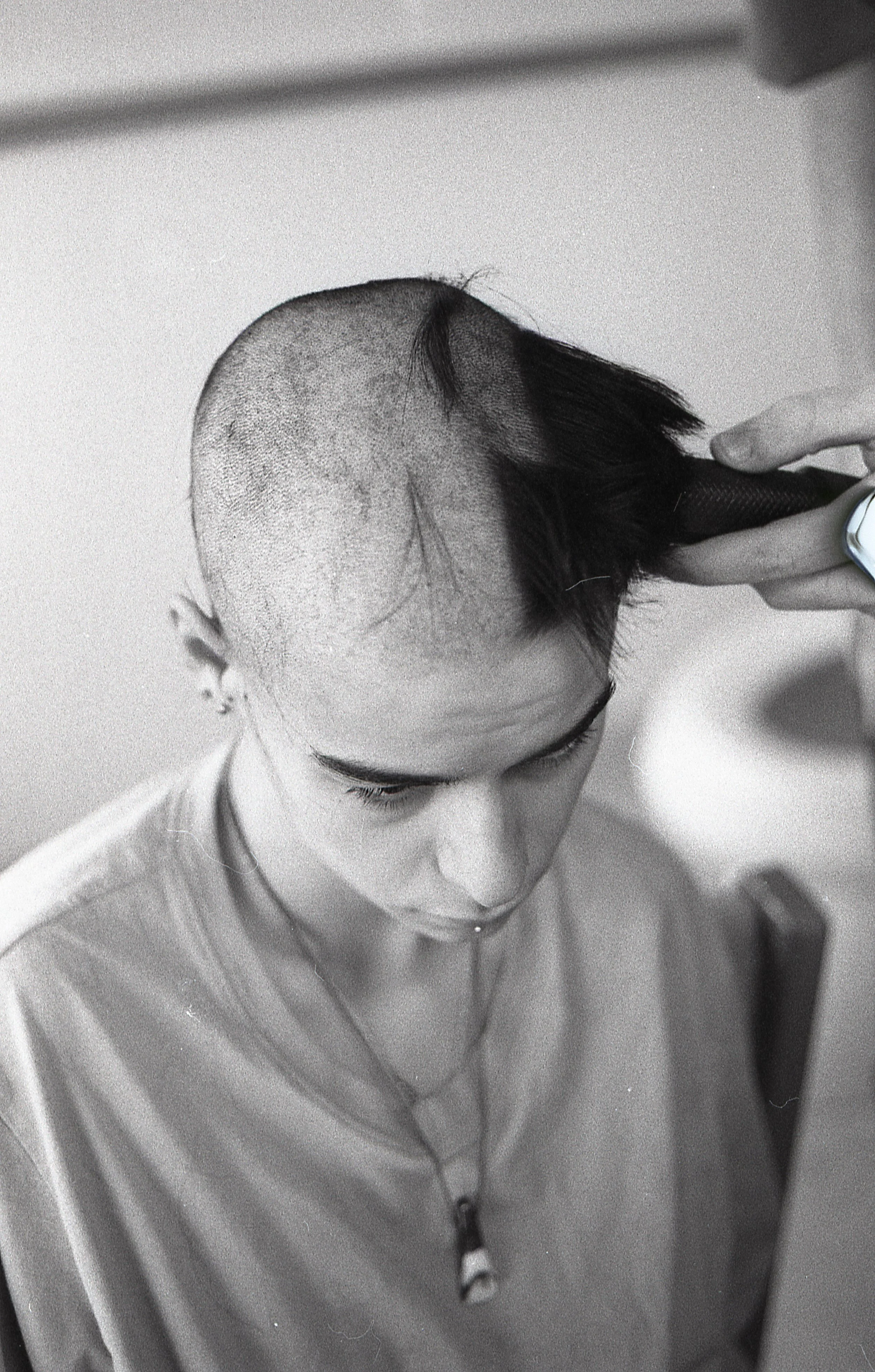 Person getting a haircut with hair clippers, bald with some hair remaining, viewed from above.
