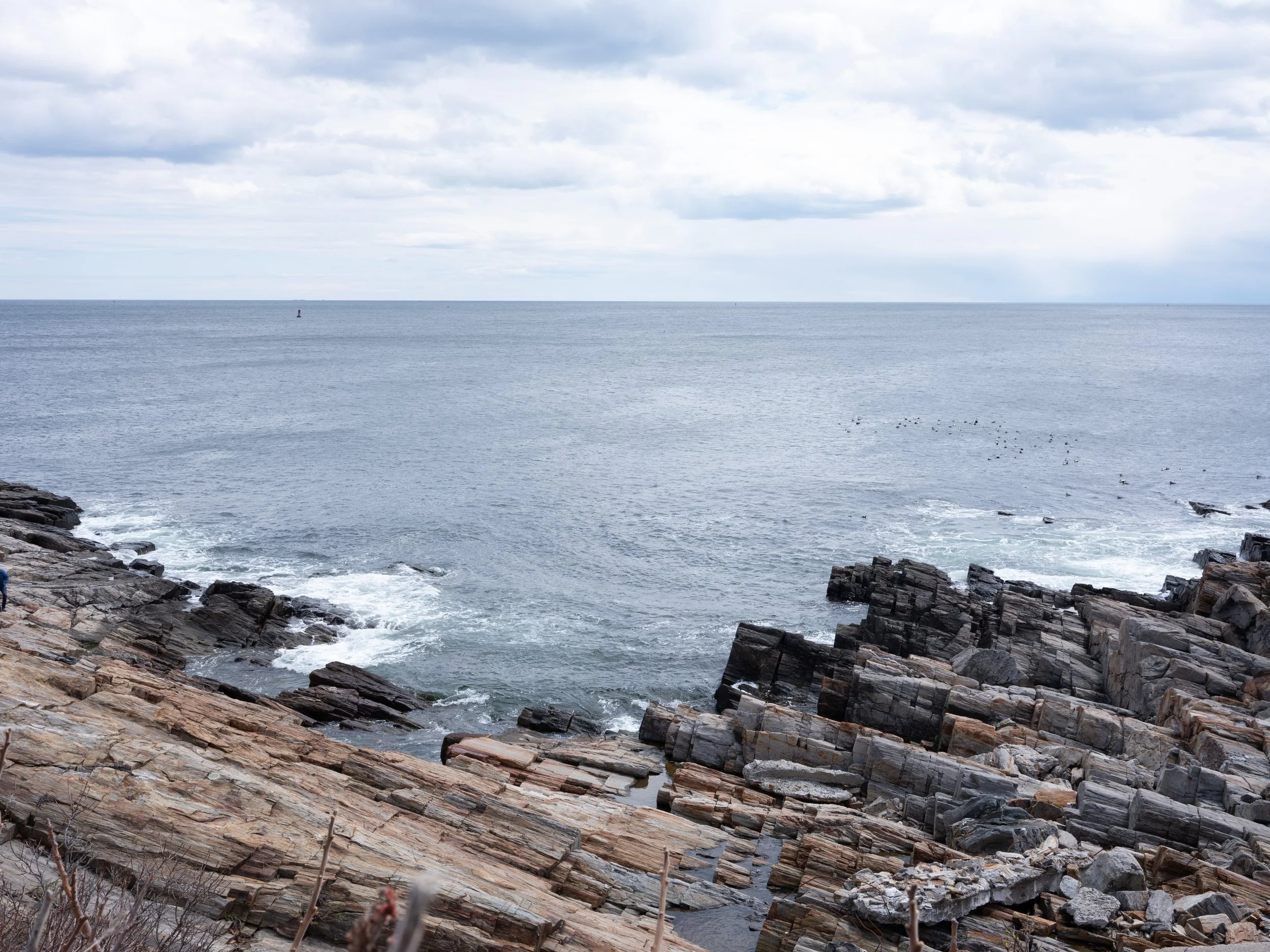 Rocky shoreline with waves crashing and overcast sky over the ocean.