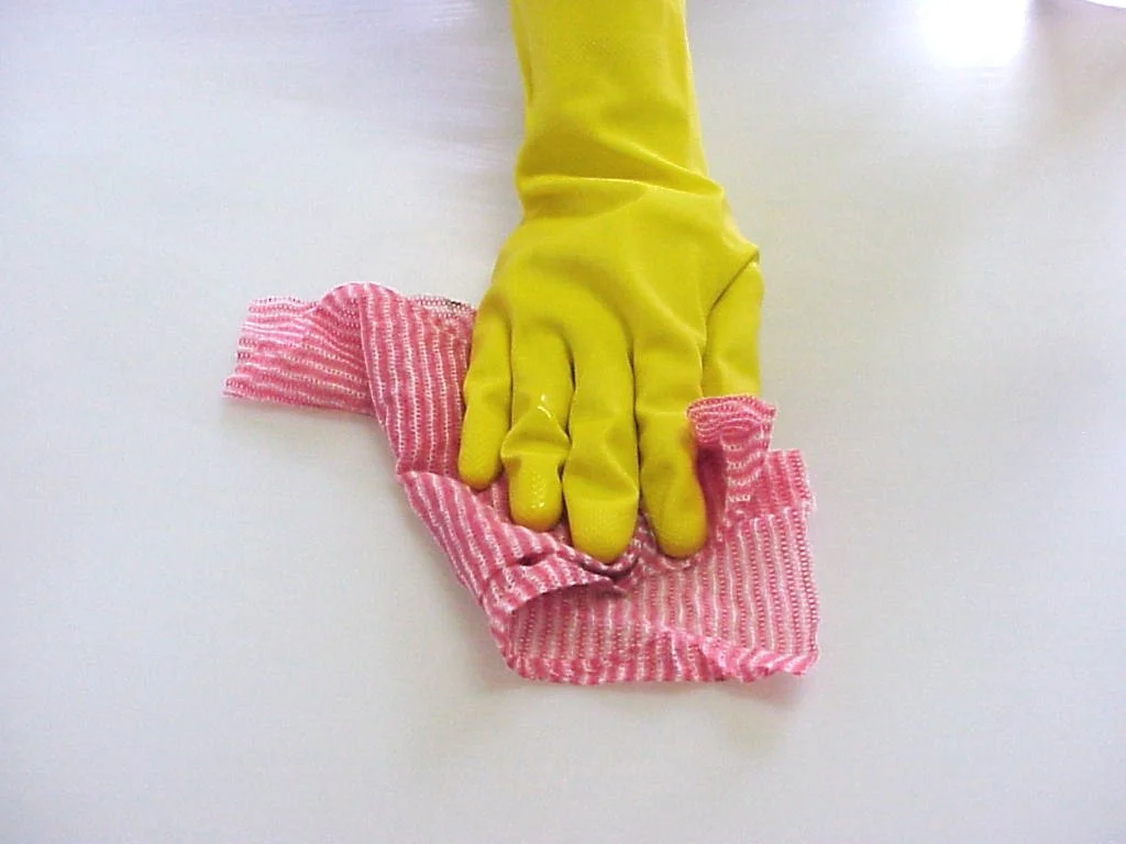 A person wearing a yellow rubber glove cleaning a white surface with a red and white striped cloth.