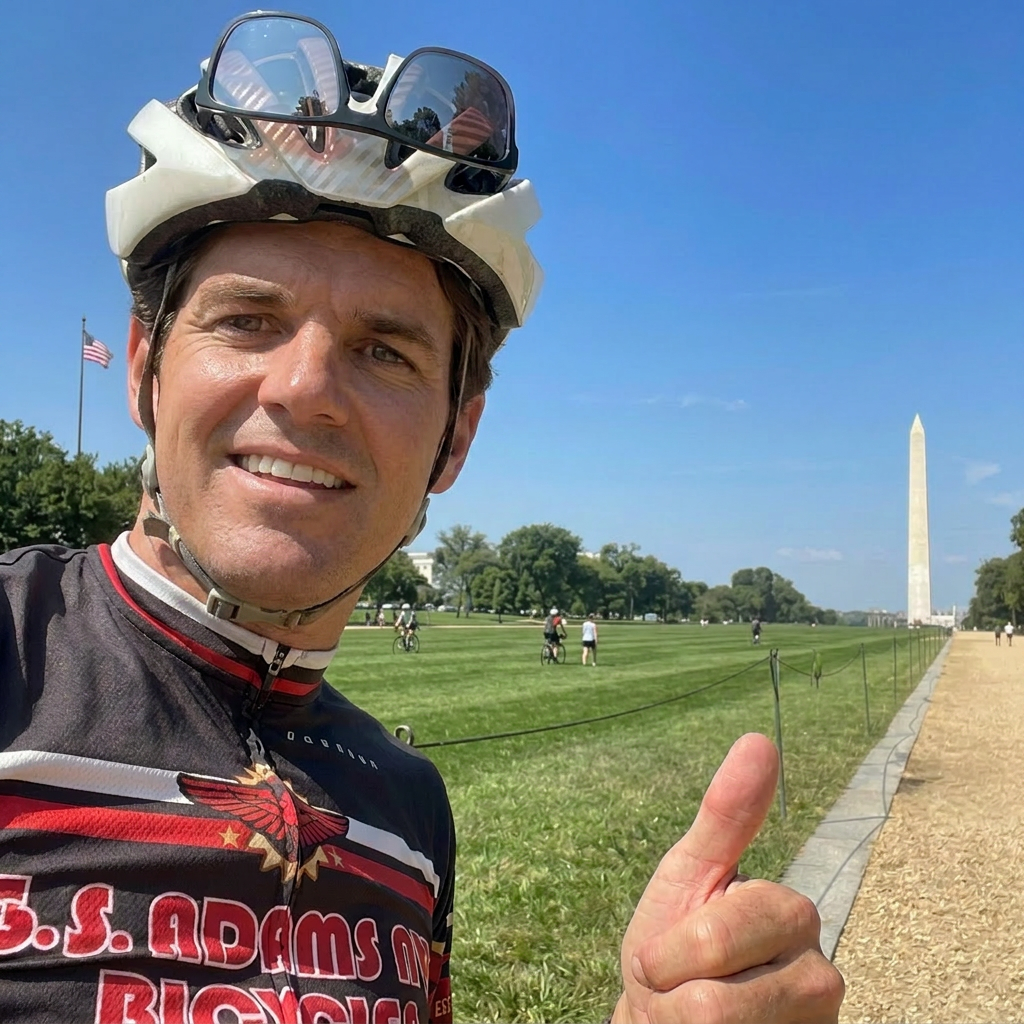 Man wearing helmet, smiling, pointing at Washington Monument in the background on a sunny day.