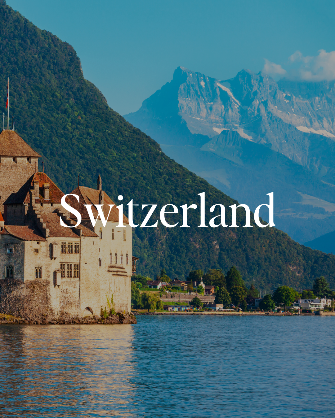 A castle on the edge of a lake in Switzerland with mountains in the background