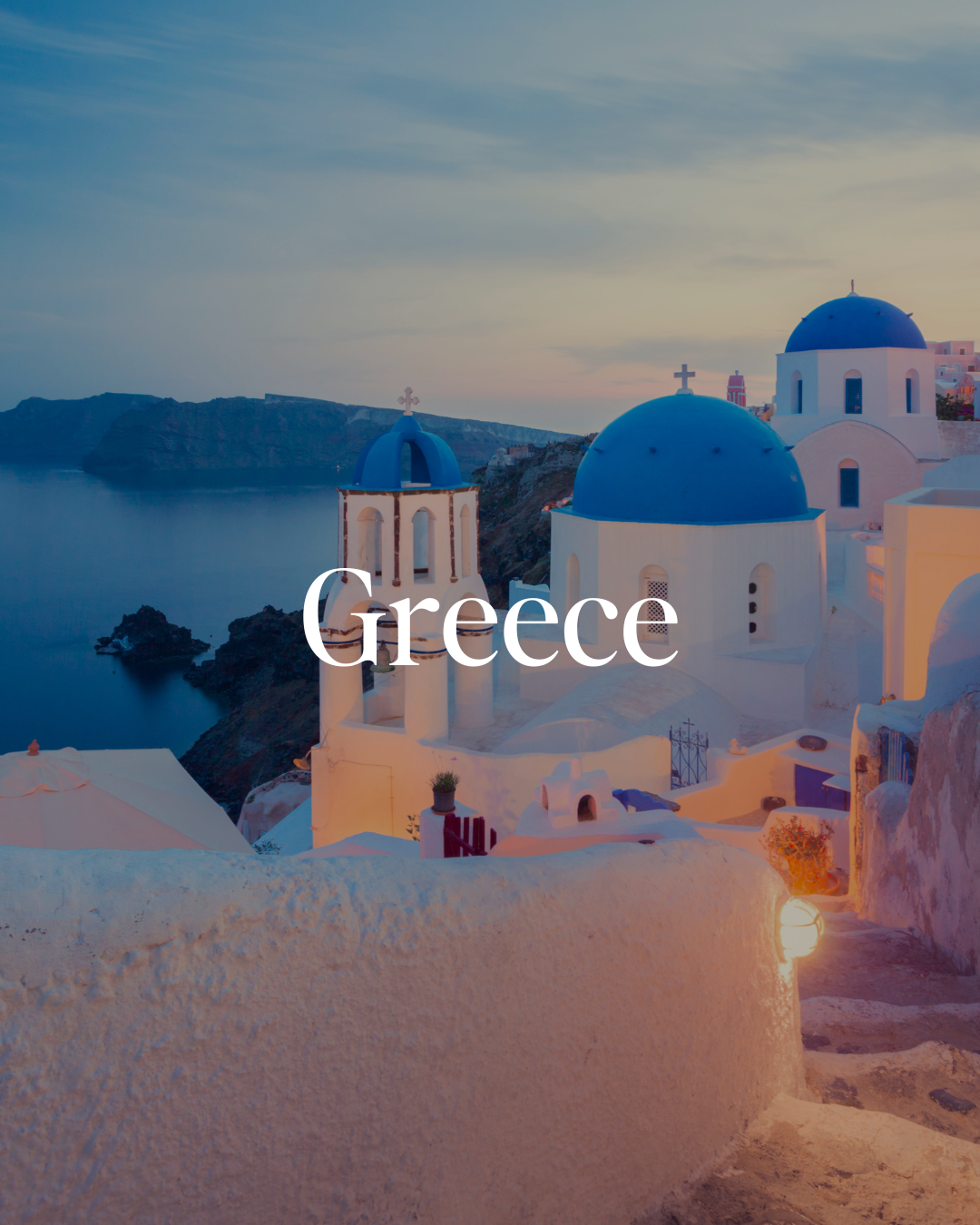 Beautiful view of Greece with white buildings and blue-domed churches overlooking the sea at sunset.