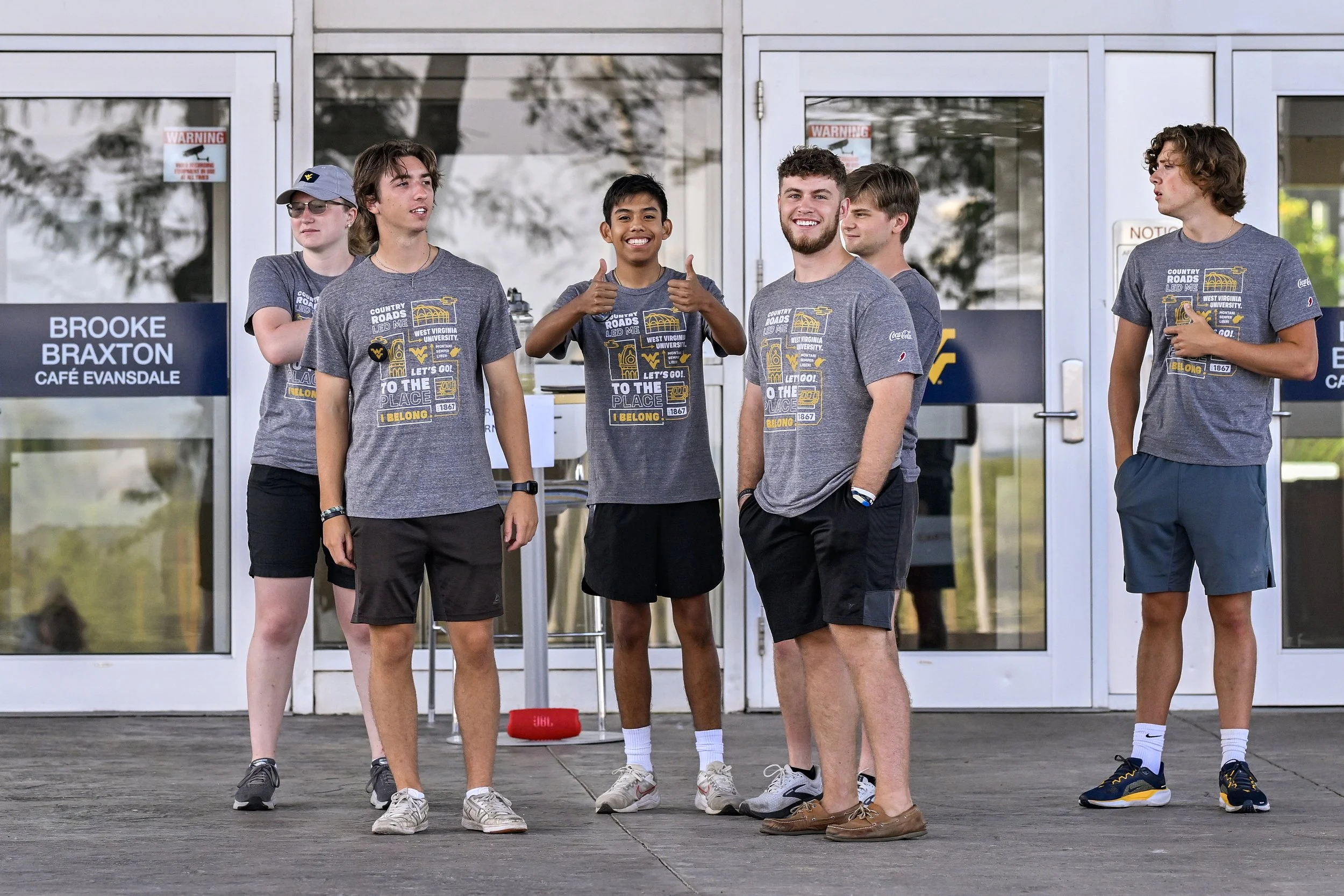 A group of boys wearing their Welcome Week shirts outside of a residence hall helping students move in