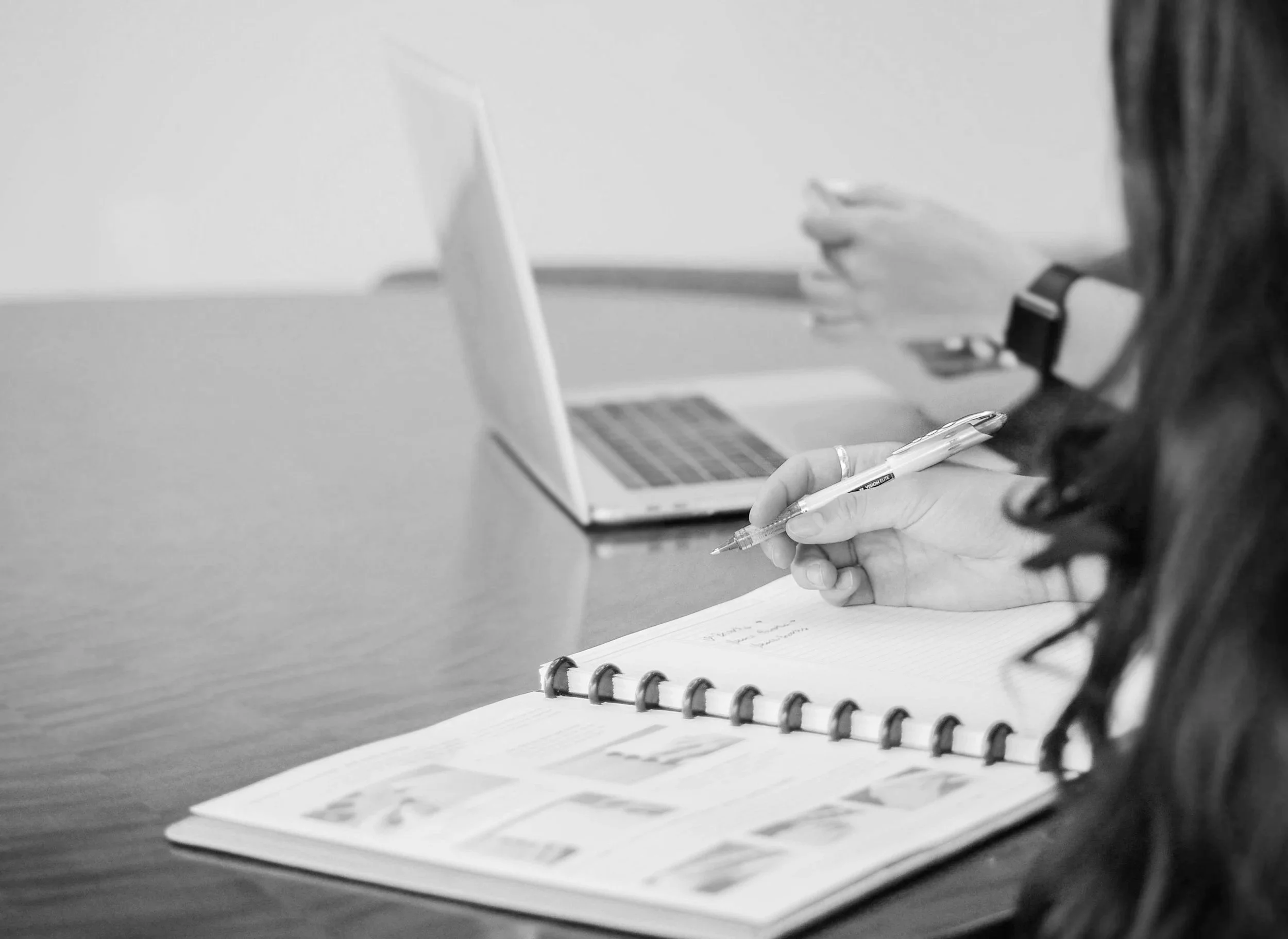 Two people working at a table with a notebook, laptop, pen, and smartphone.