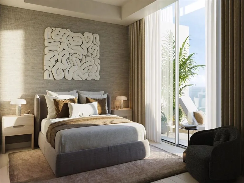 A modern bedroom with a large bed, nightstands, lamps, and a balcony with sliding glass doors and outdoor seating overlooking greenery.